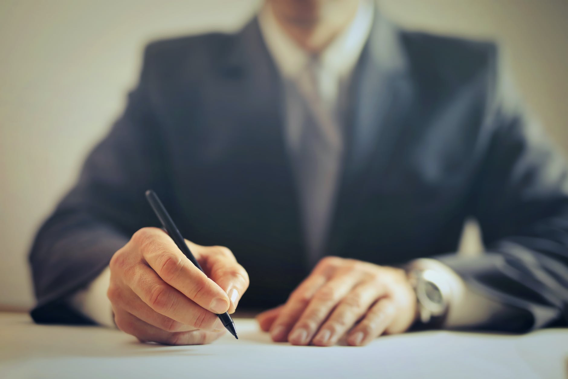 Indvidual wearing blue suit and tie and writing with pen.