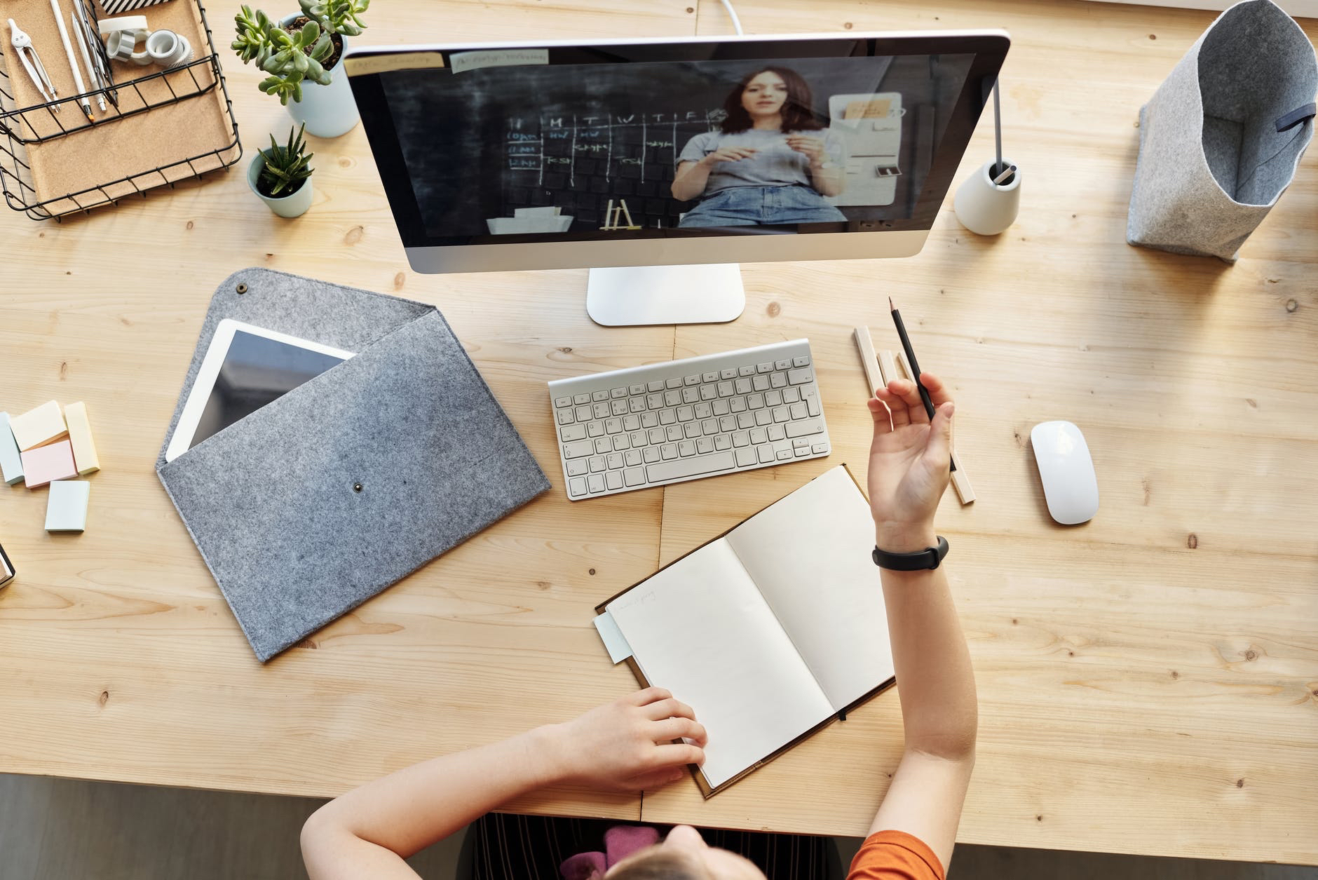 Desktop computer monitor and desk with hand holding pencil and taking notes.