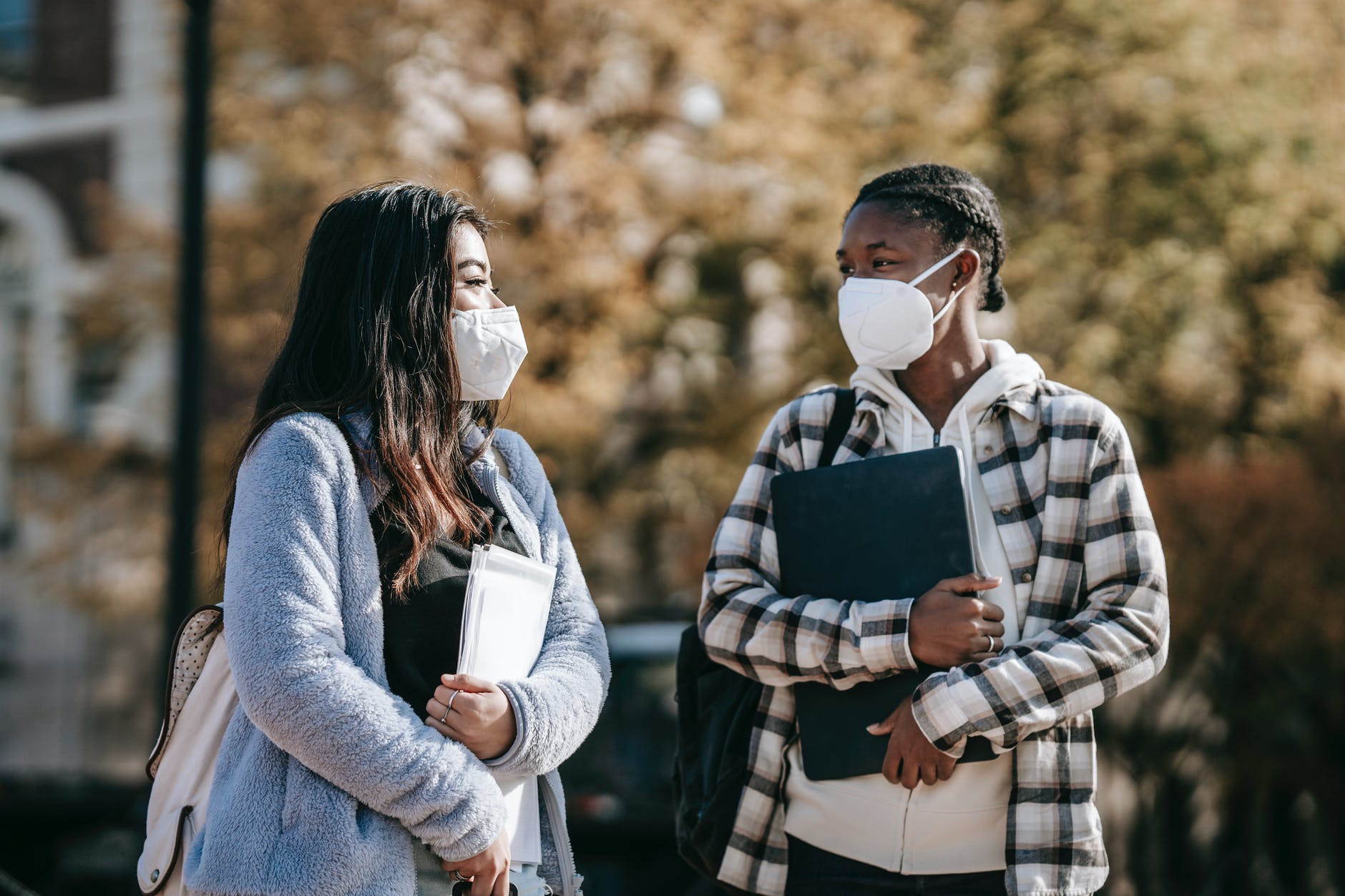 Two black students wearing masks and holding books walk together.
