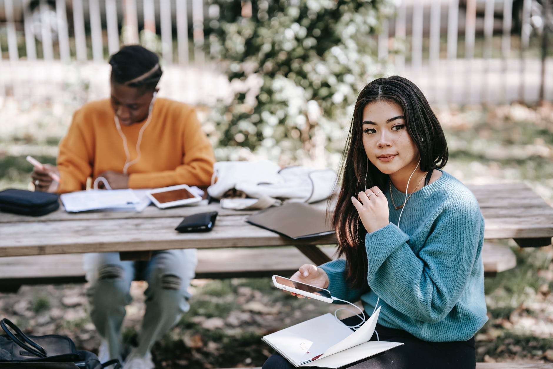 Photo of two students wearing earphones at picnic table with books and notes.