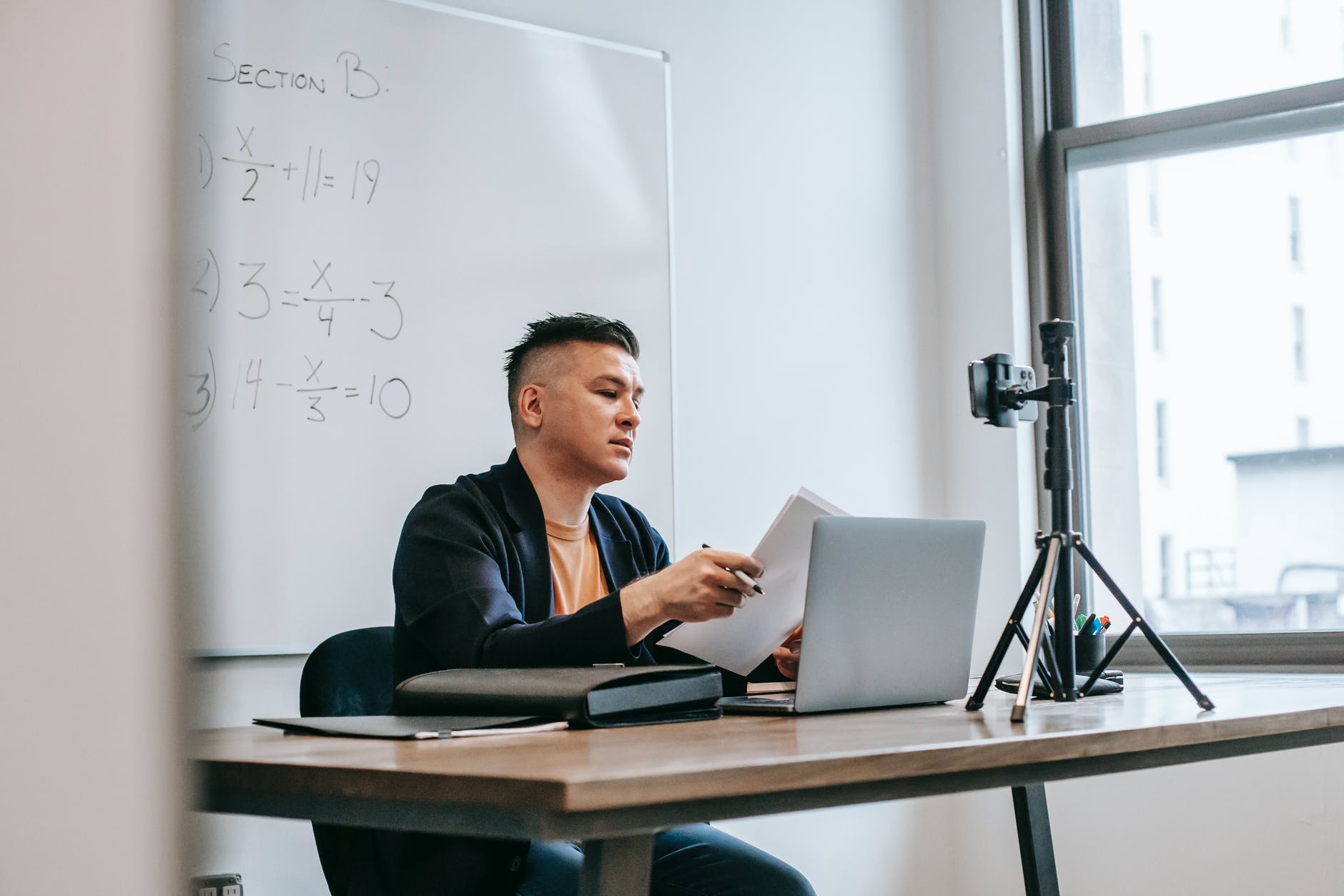 Instructor at desk with laptop and phone mounted on tripod.