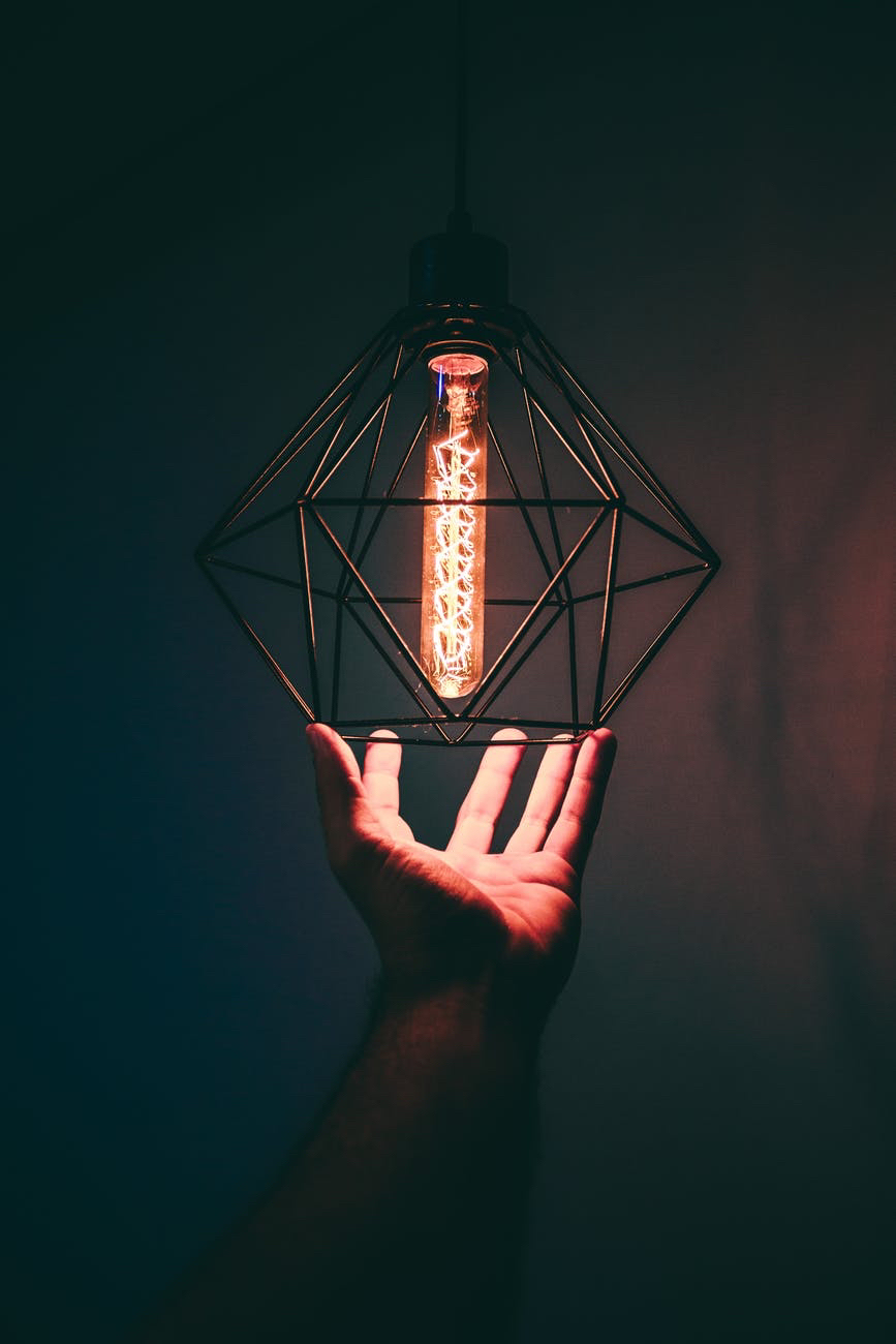 Hand holding lightbulb inside wireframe holder.