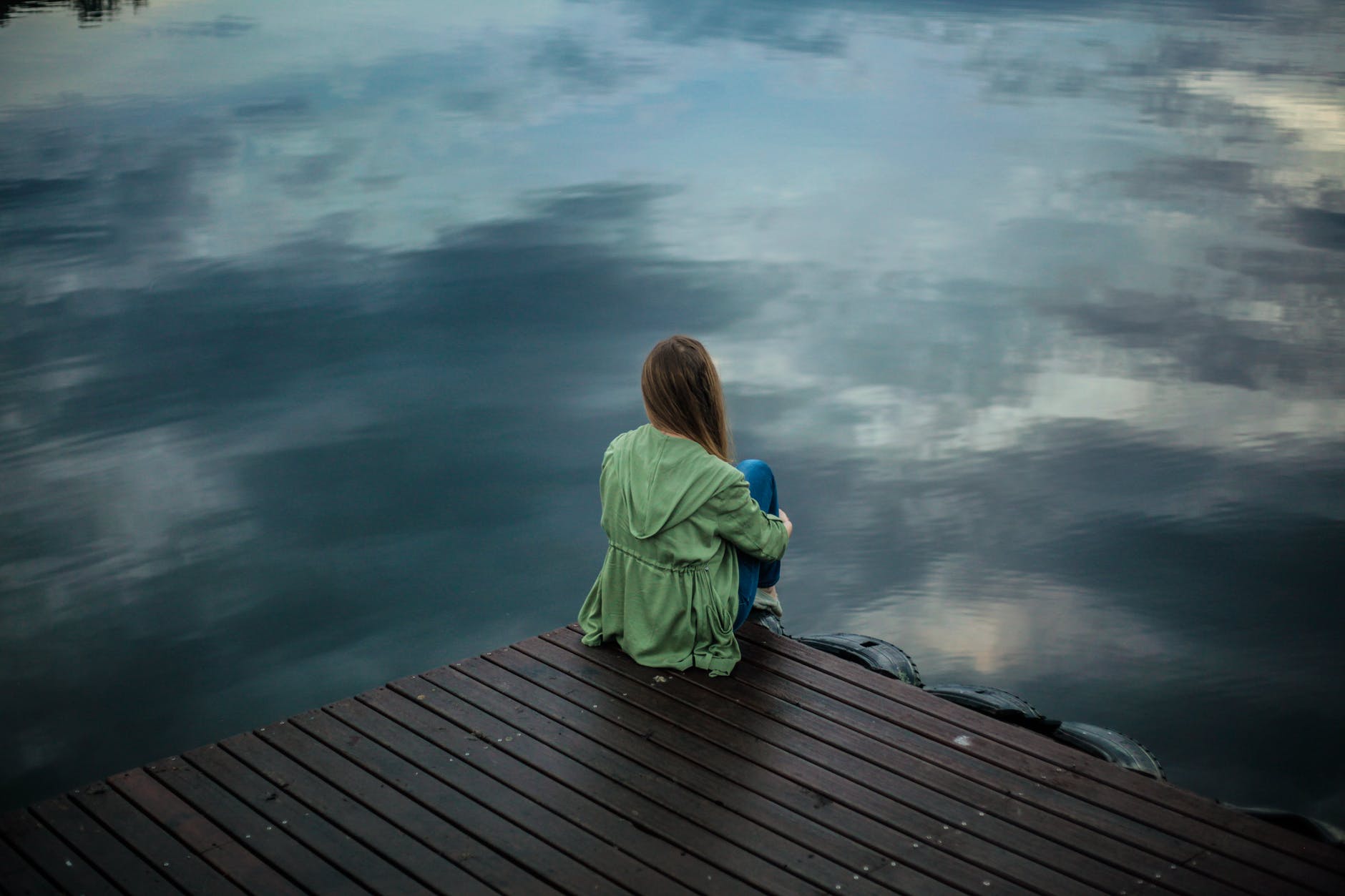 Woman facing water sitting on dock.