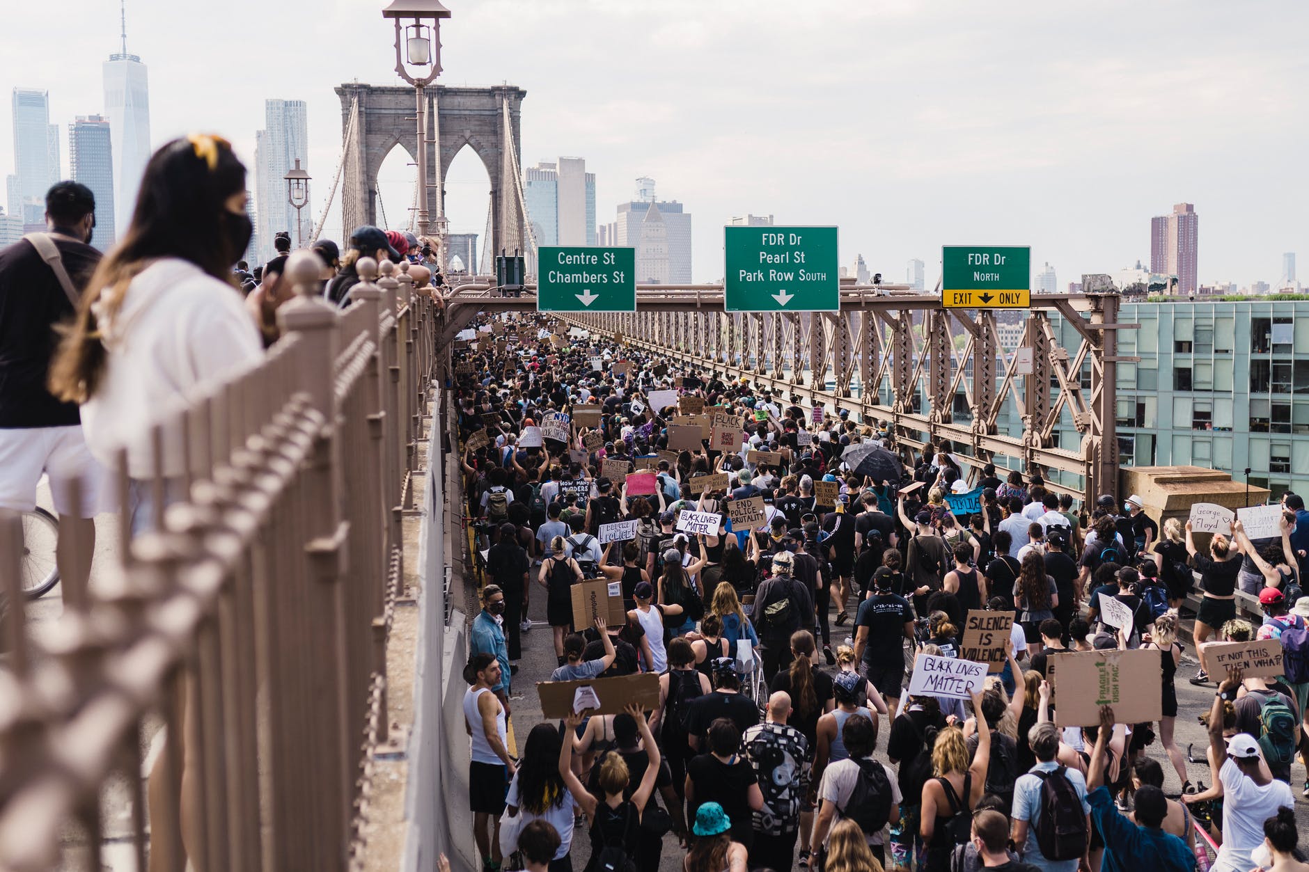 People walking on bridge in protest wearing masks and holding signs.
