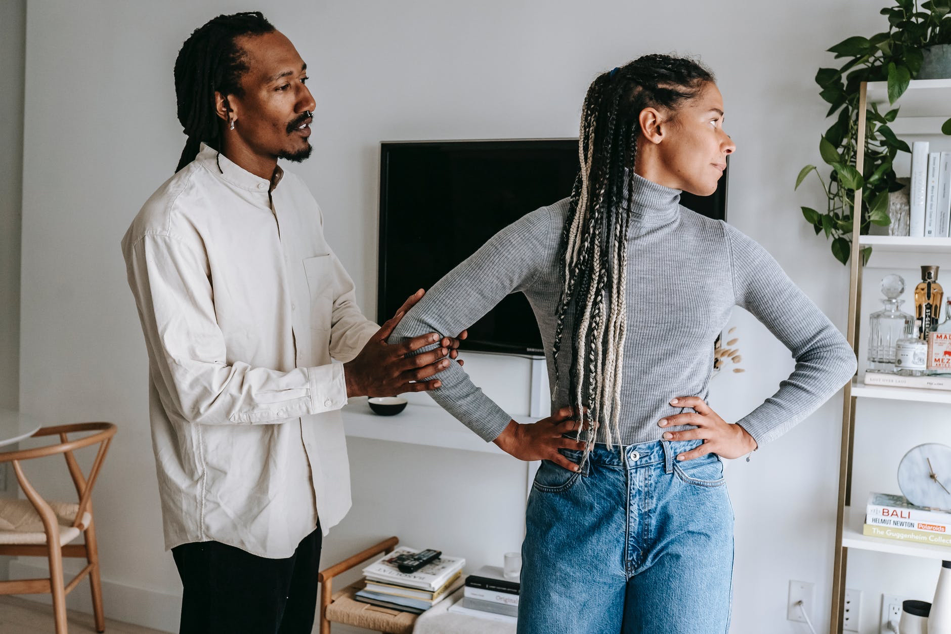 Black man holding elbow of black woman with long braided hair looking away.