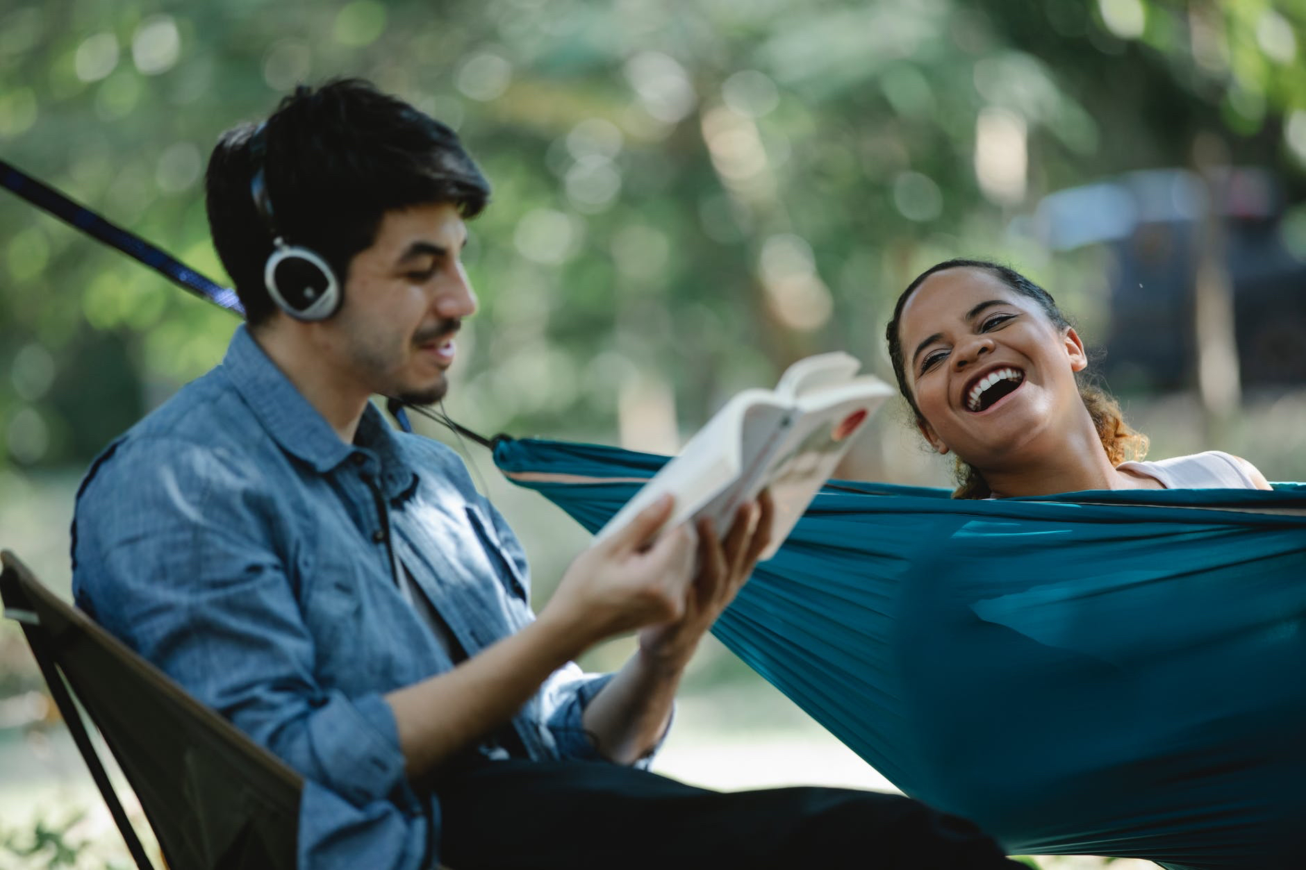 Latinx student with mustache and wearing headphones and reading book next to young woman laughing 