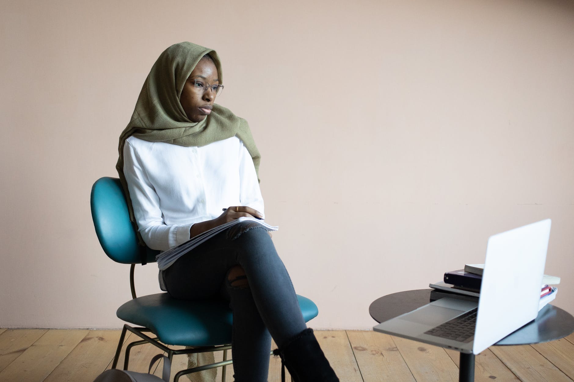Black woman wearing headscarf and seated in chair in front of laptop.