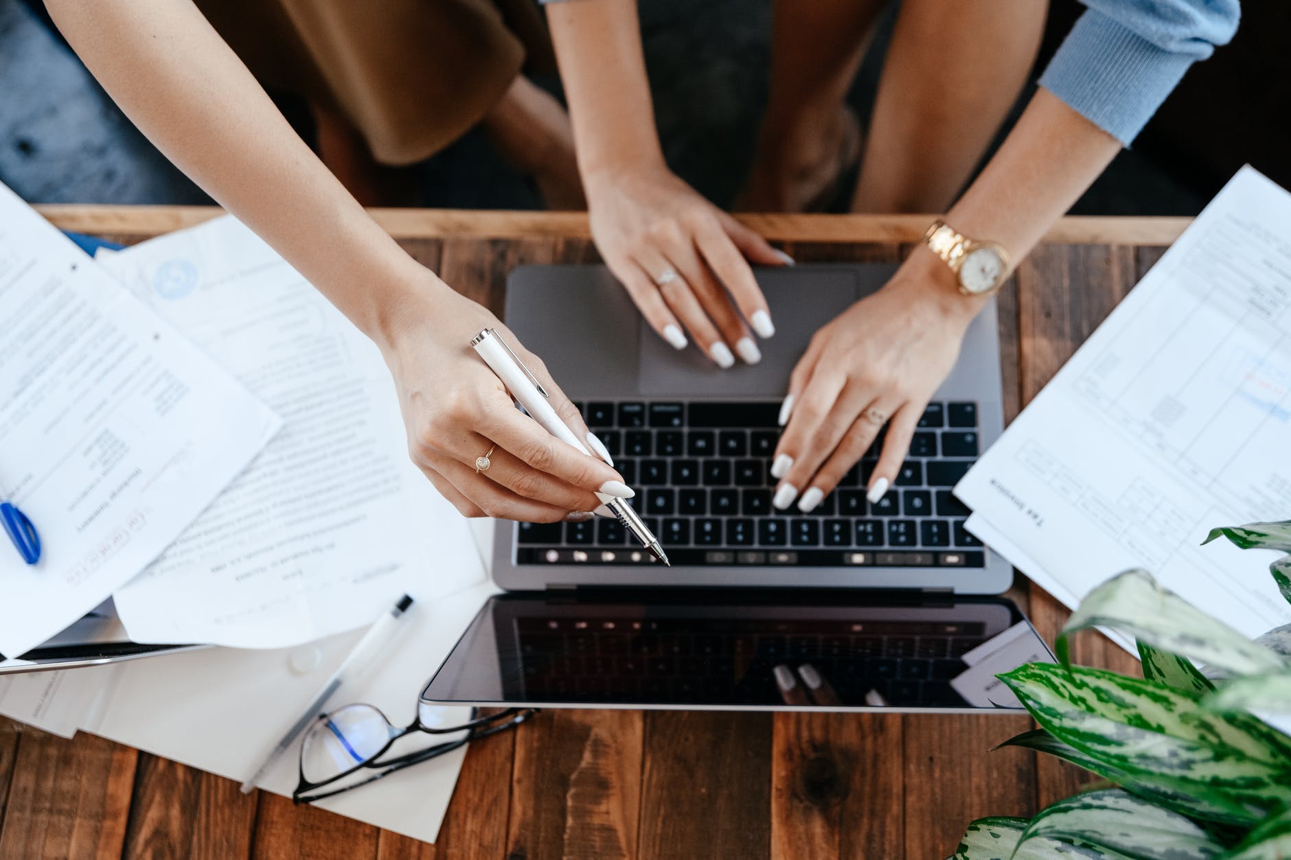 Several hands over laptop keyboard. One hand is holding a pen.