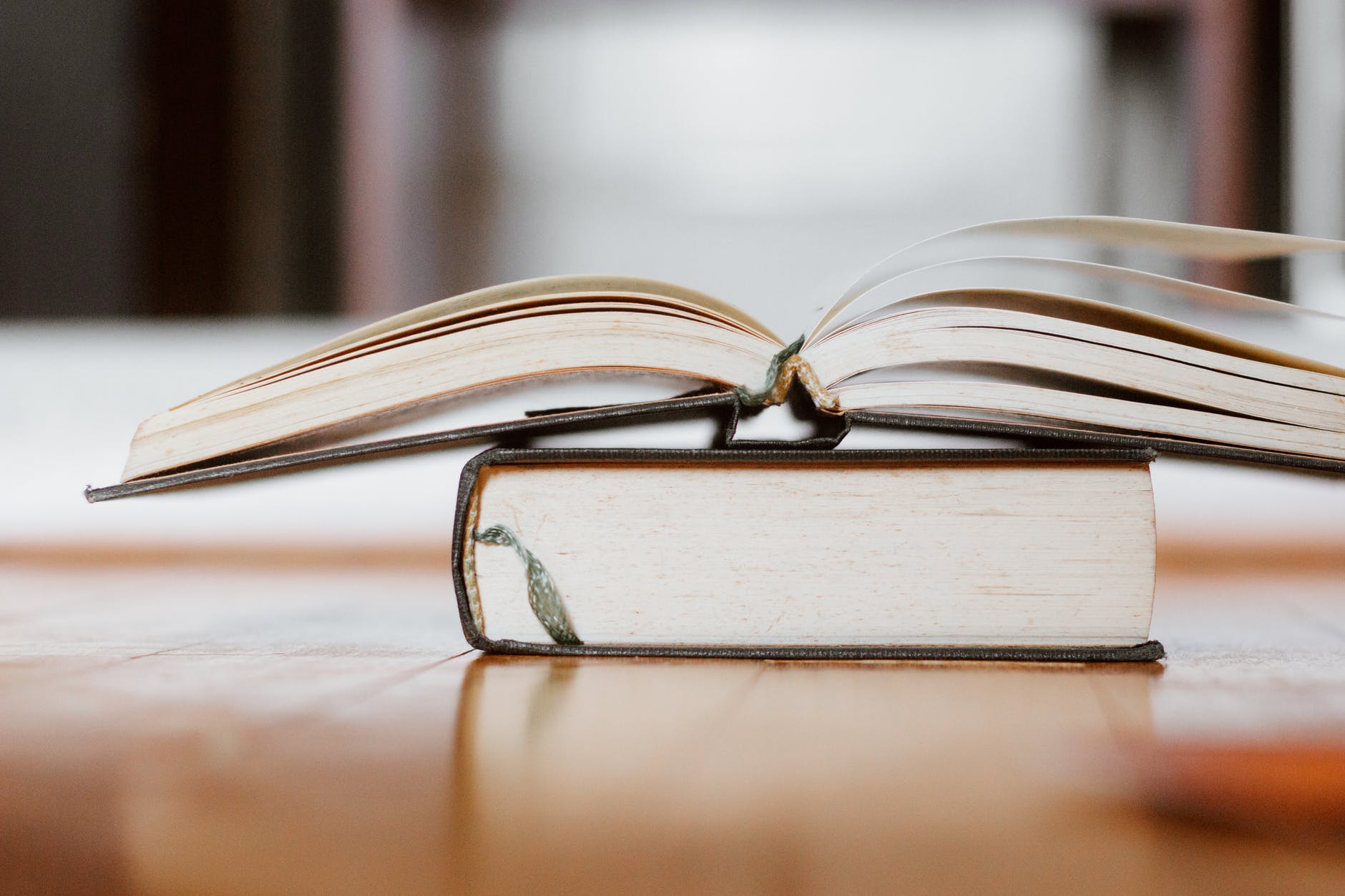 Open book on a table on top of a closed book. Both books are hardcovers.