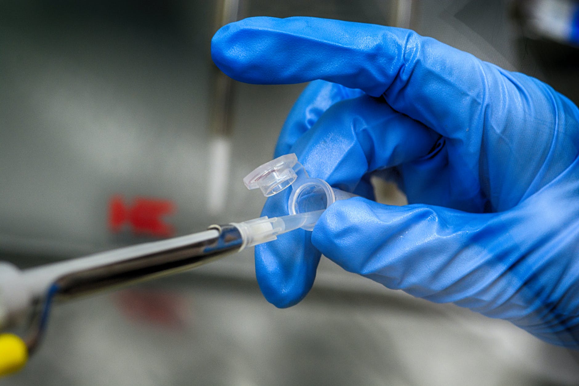 Gloved hand holding open microfuge and tip of pipettor and transparent plastic tip with clear liquid.