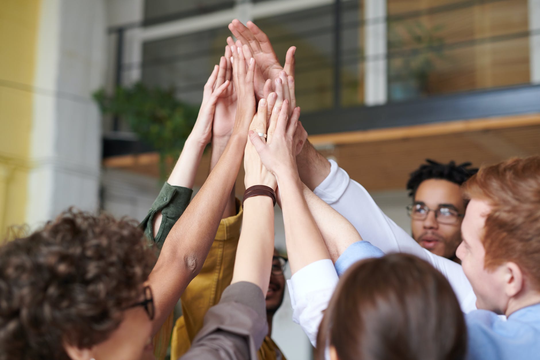 Five people in a group giving each other a high five. Hands are meeting in the air above the heads of the five people facing each other.