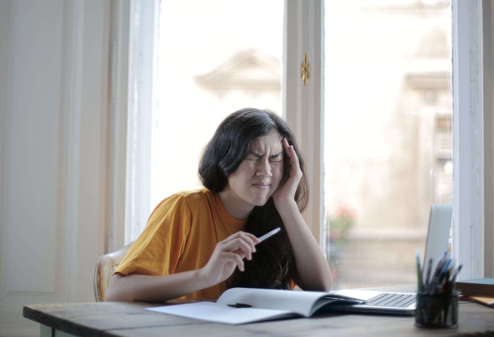 Student in front of laptop and notebook with hand on forehead closing eyes in frustration.