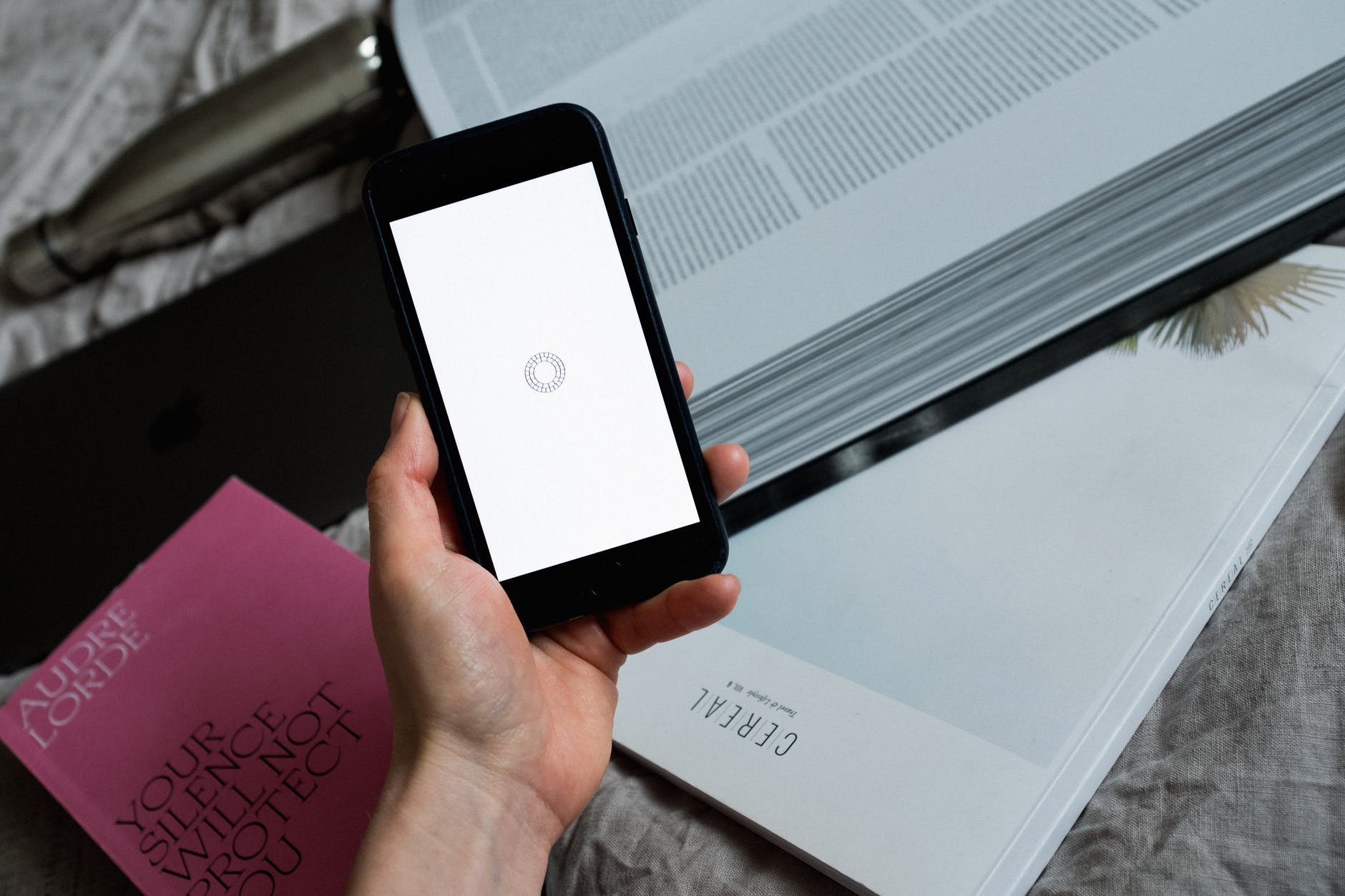 Smartphone with white screen held by hand. In the background, an open book is visible.