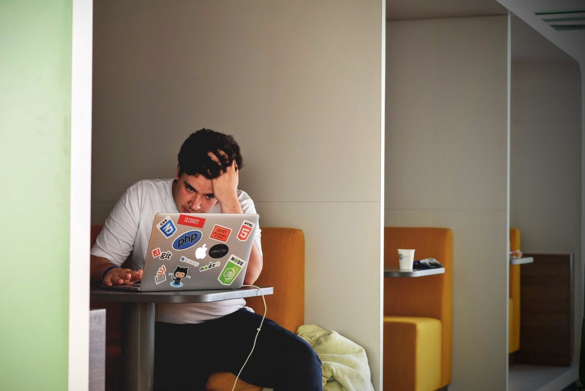 Man in small room working with computer holding head and staring at screen. Man looks distressed.