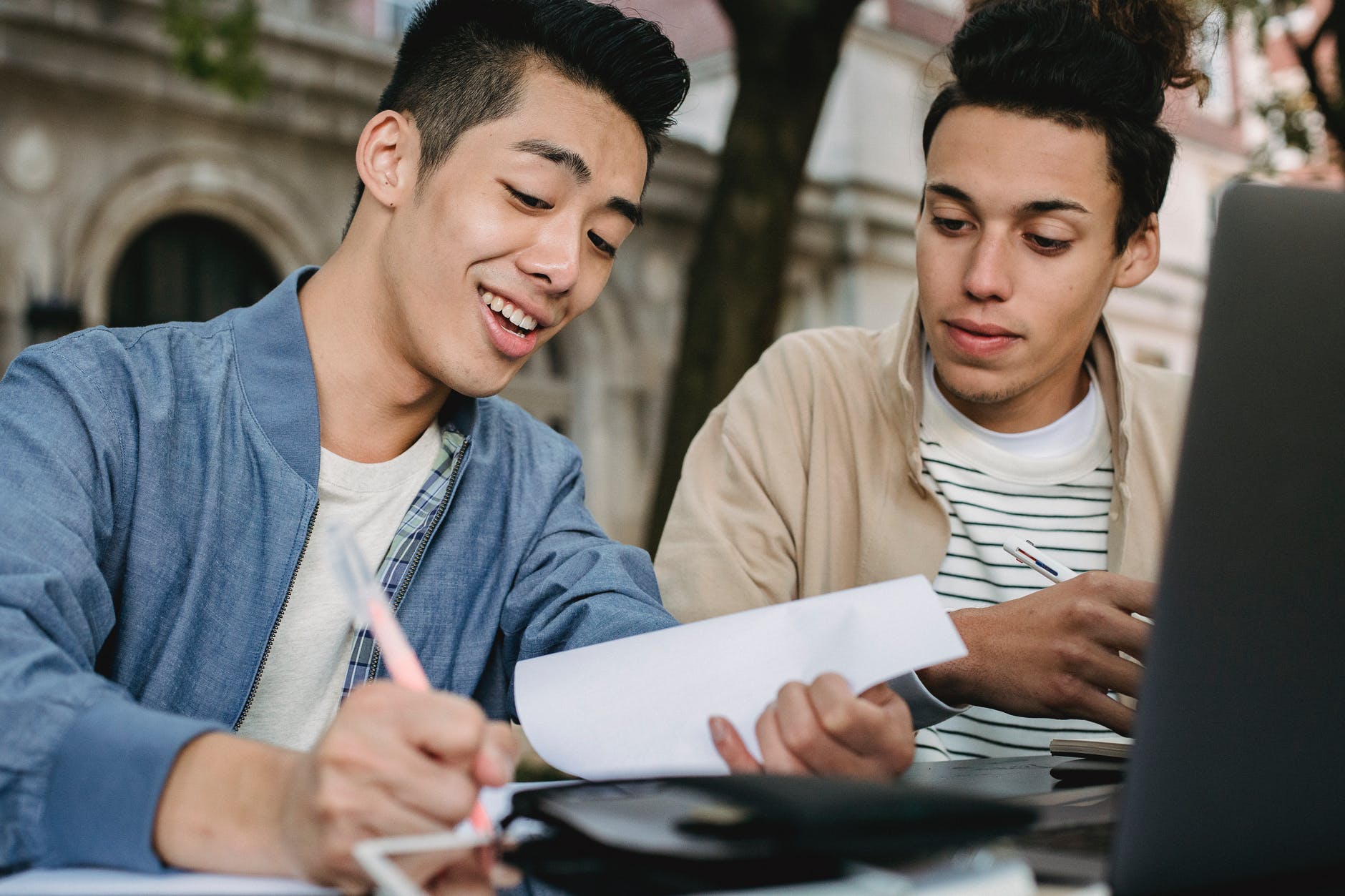 Two men with pens with the one on the left writing.