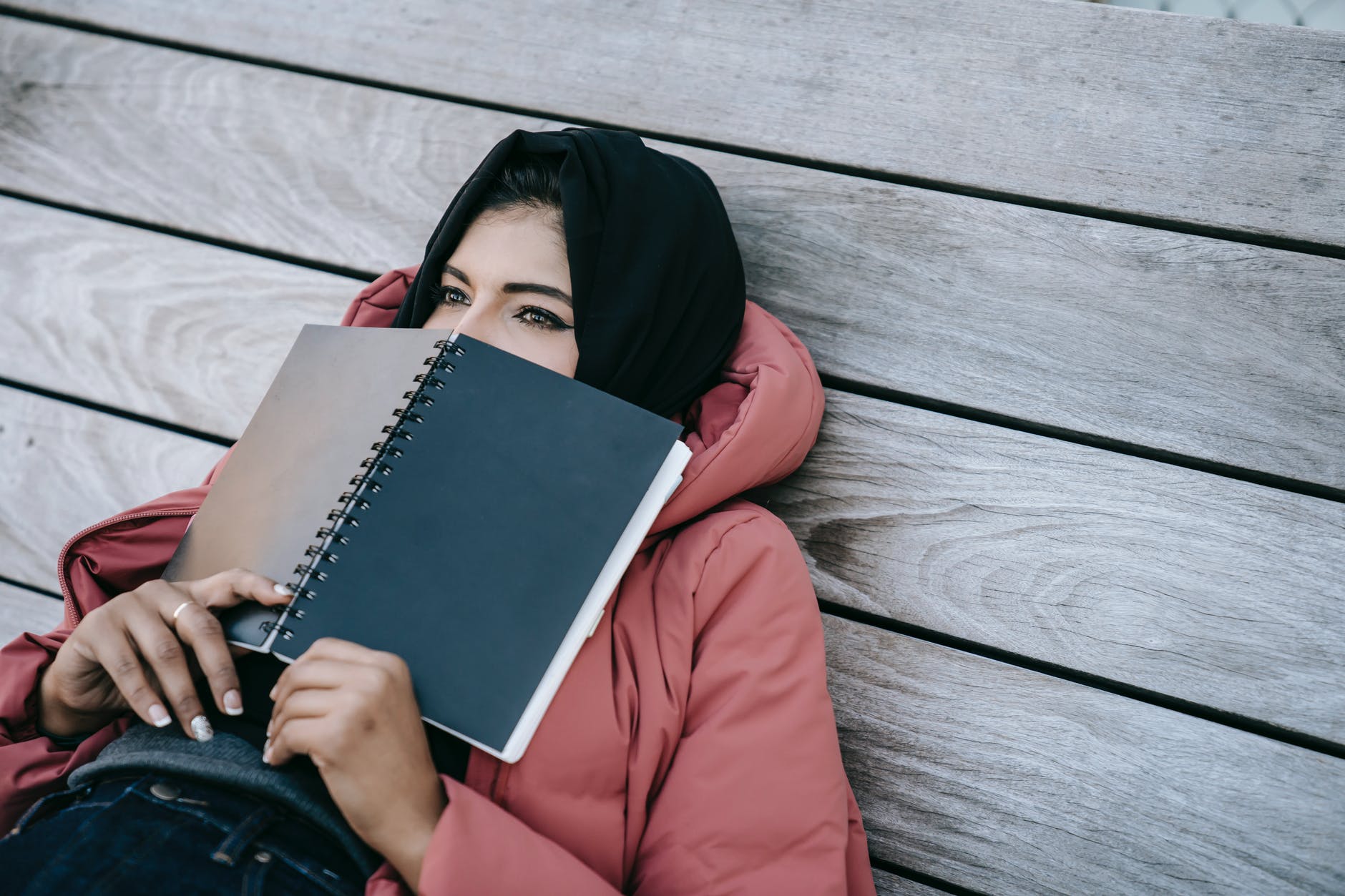 Woman with black headscarf holding black notebook covering mouth.