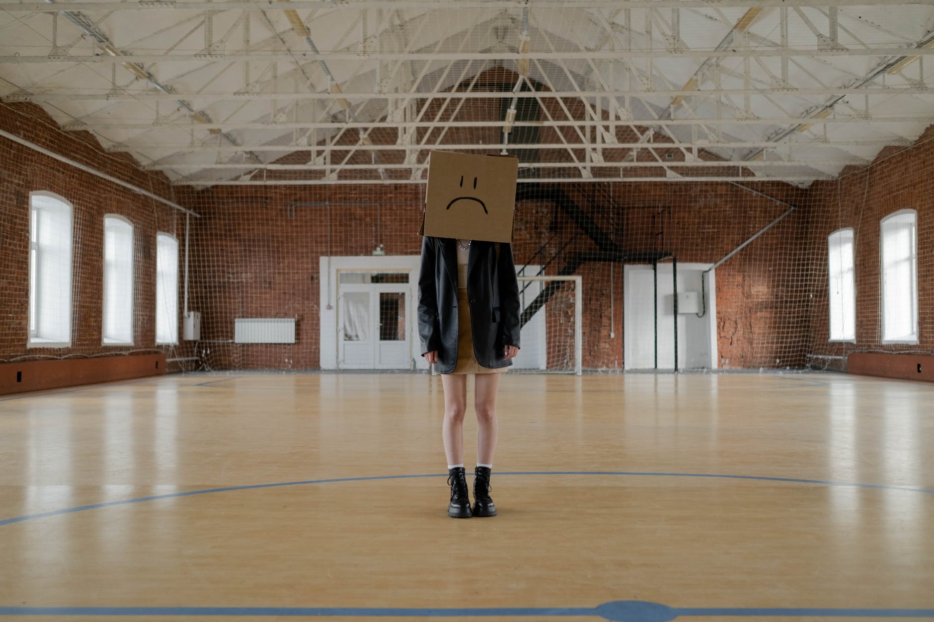 Empty gymnasium with person wearing dress and cardboard box with frowny face.