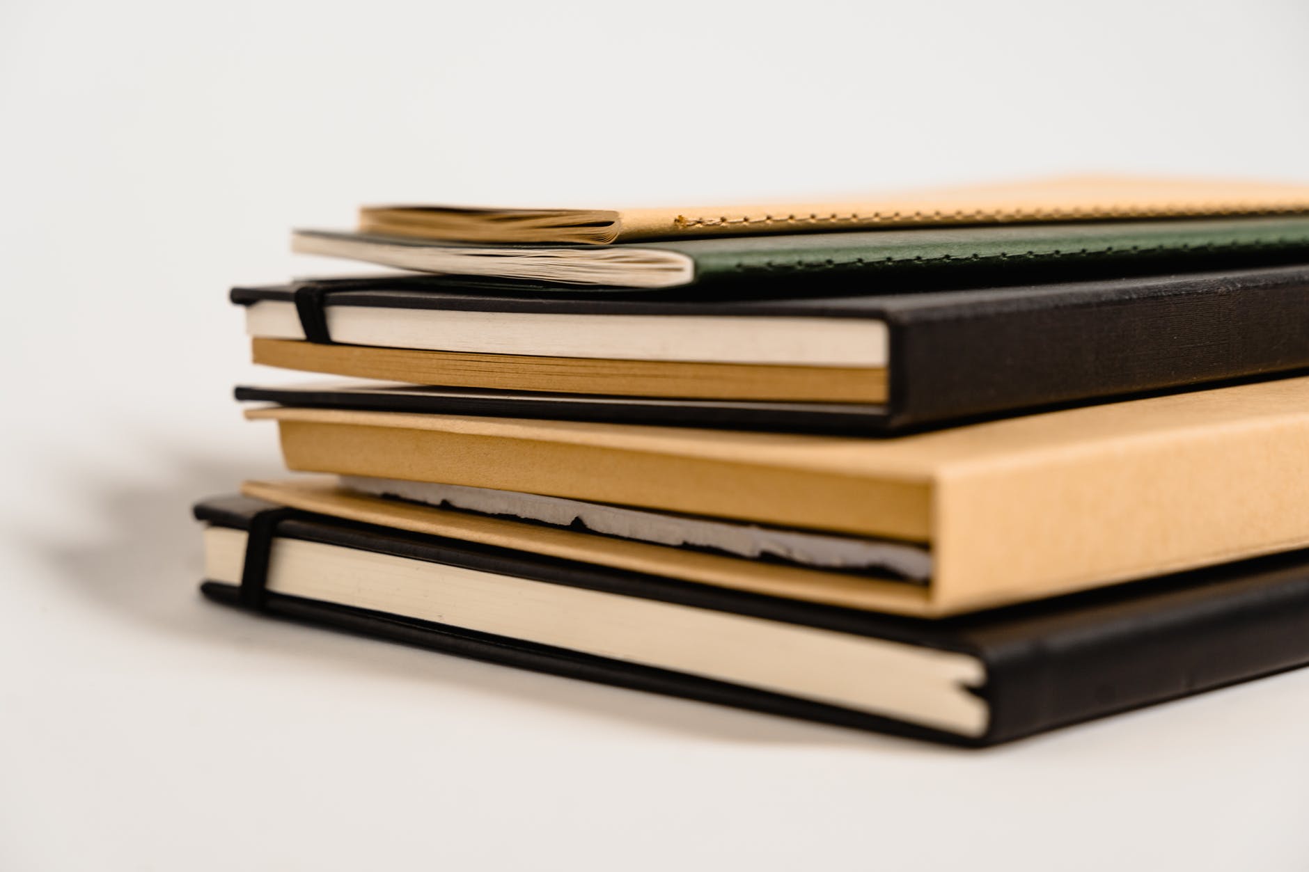 Stack of hardcover books with beige and black covers. Two slim books on top (beige and black) Followed by a black, a beige, and another black book on the bottom.