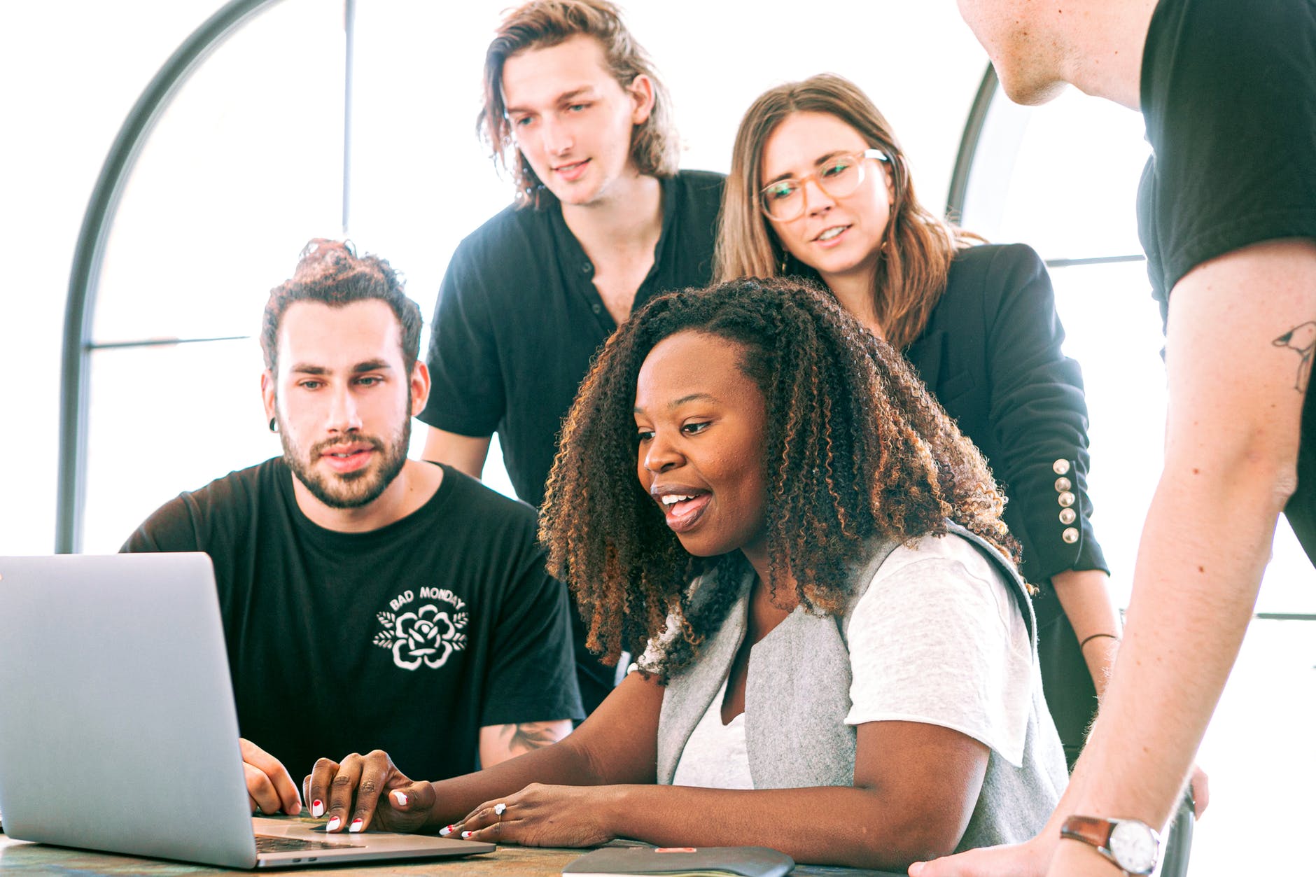 Group of people surrounding black woman with curly hair working on laptop. Everyone is focused on the screen. The woman's mouth is open.