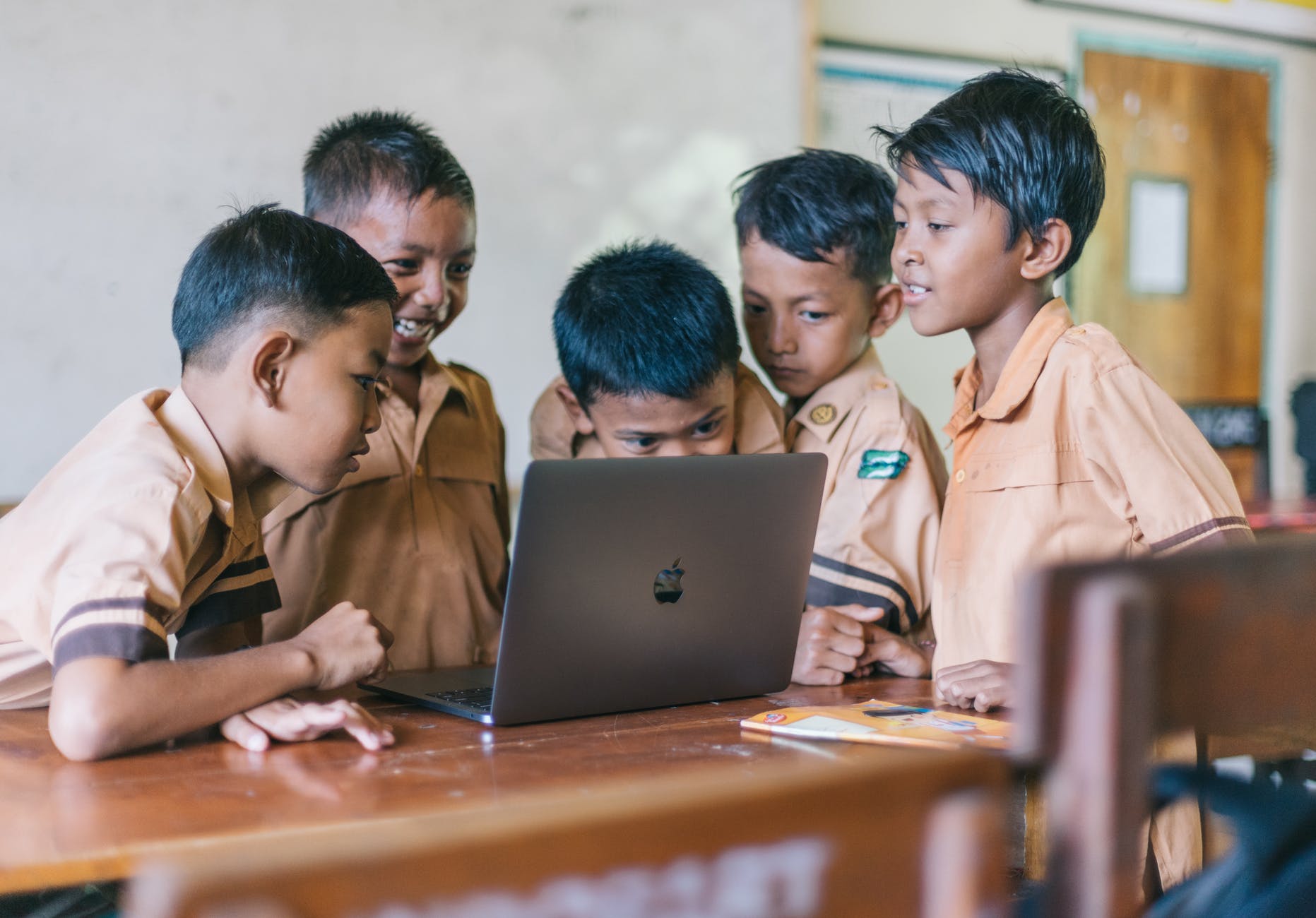 Several students with black hair and brown skin surrounding open laptop.