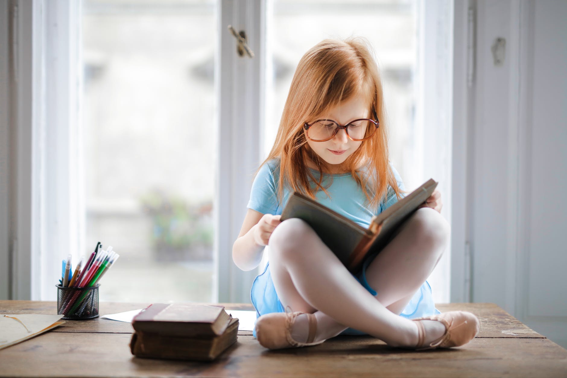 Girl with glasses and red hair sitting and reading book.