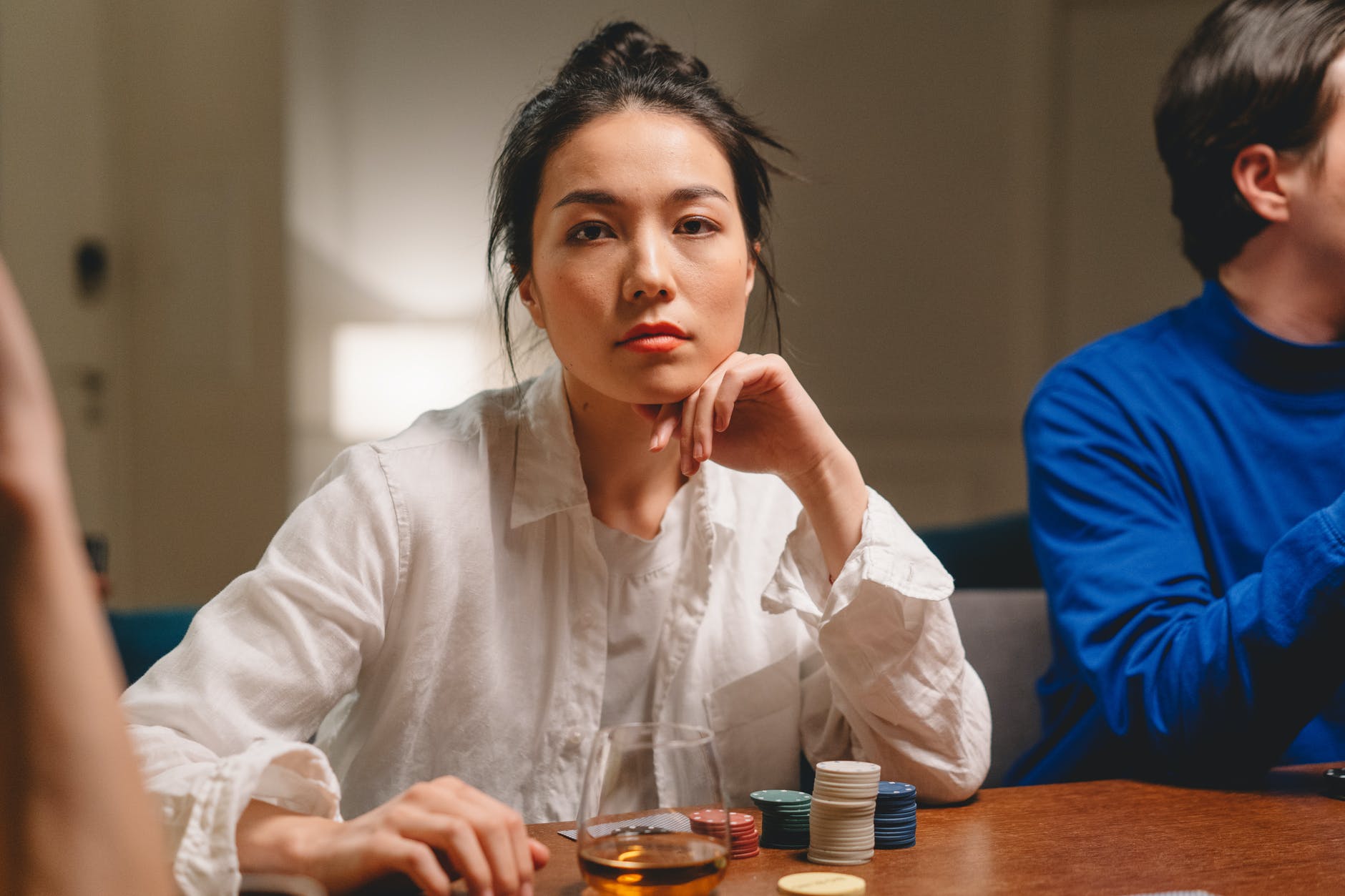 Woman wearing white button up shirt seated at table with poker chips (tokens).