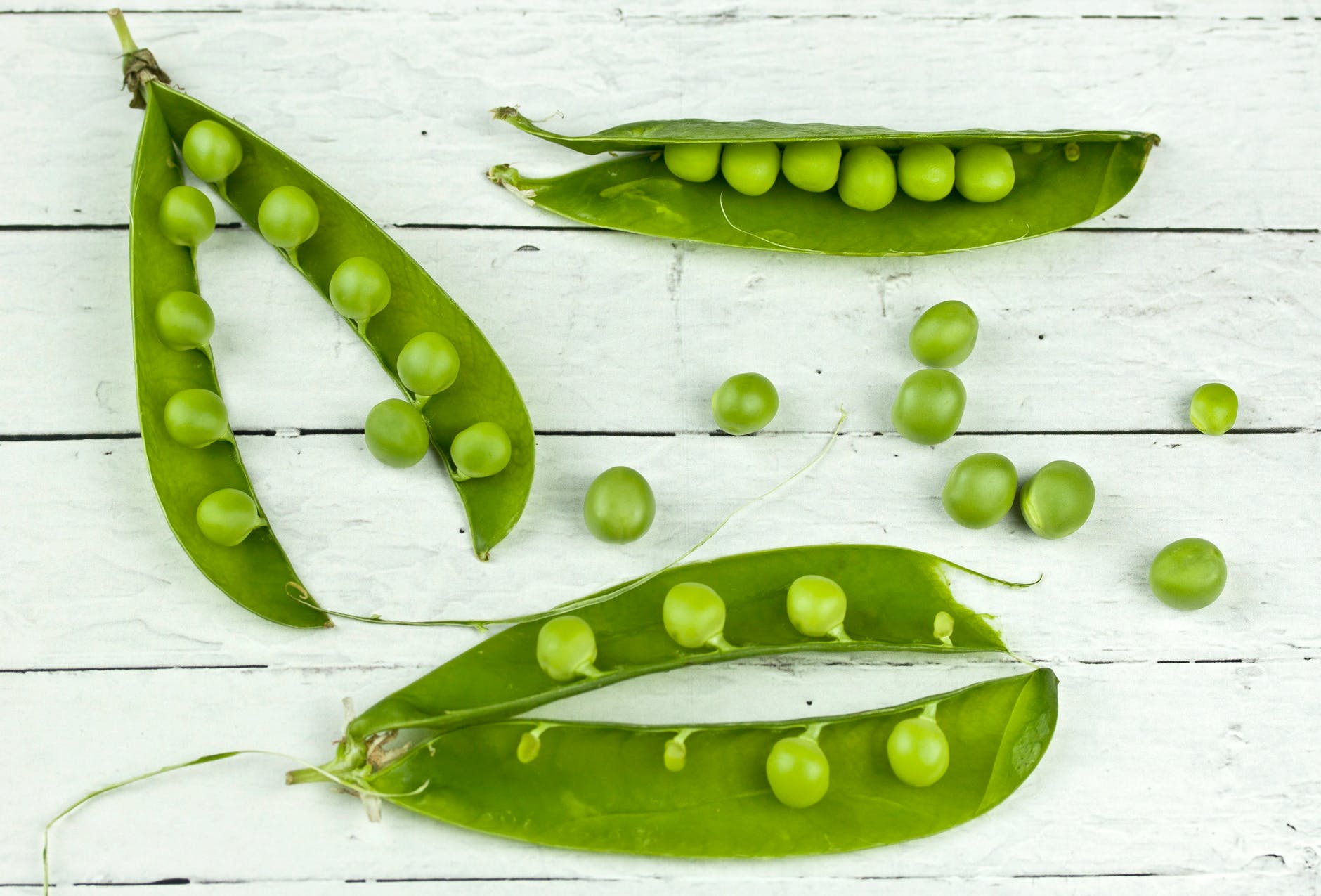 Five pea pods and several green peas on a white table.
