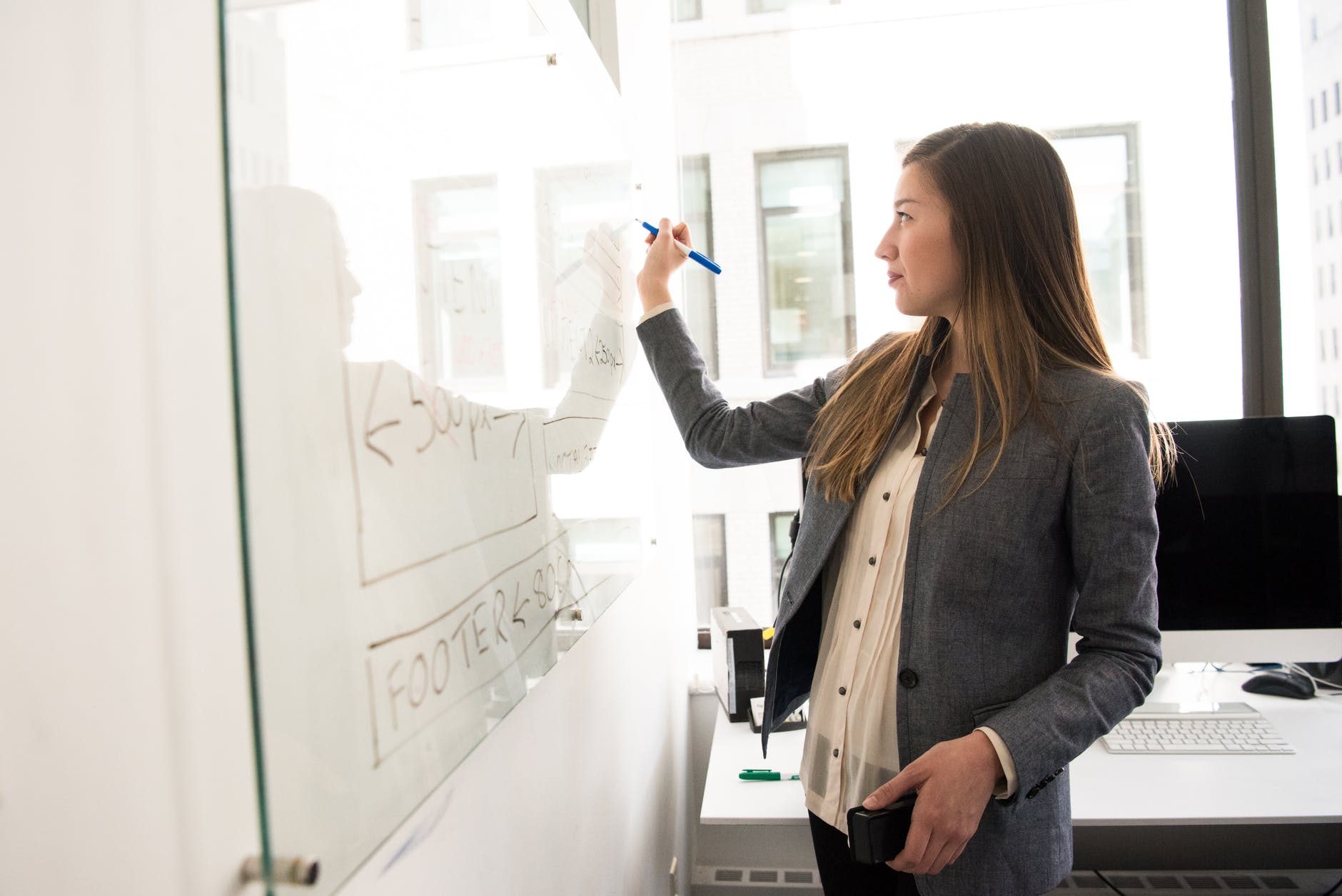 Woman holding dry erase marker and writing on whiteboard.