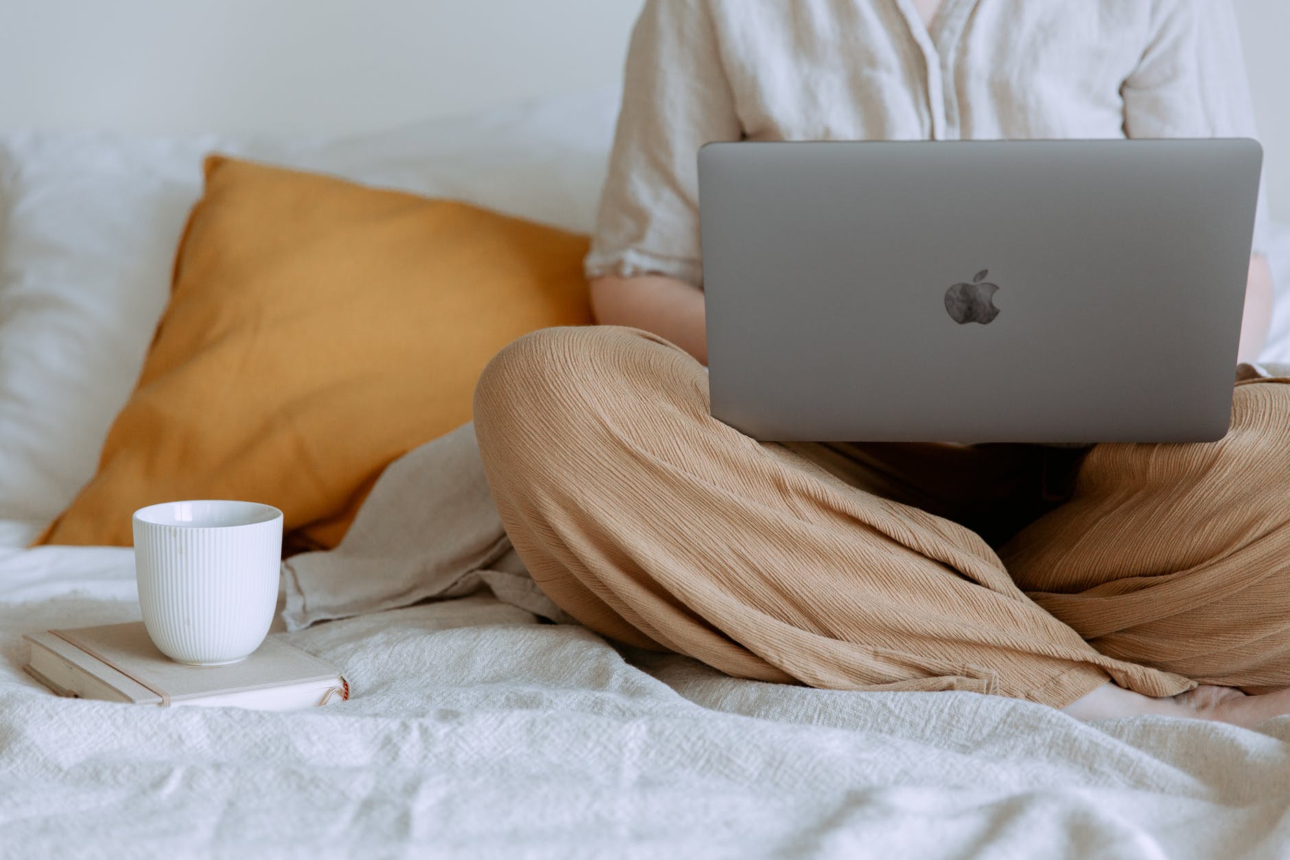 Gray Mac laptop on knees of person in bed with cup of tea