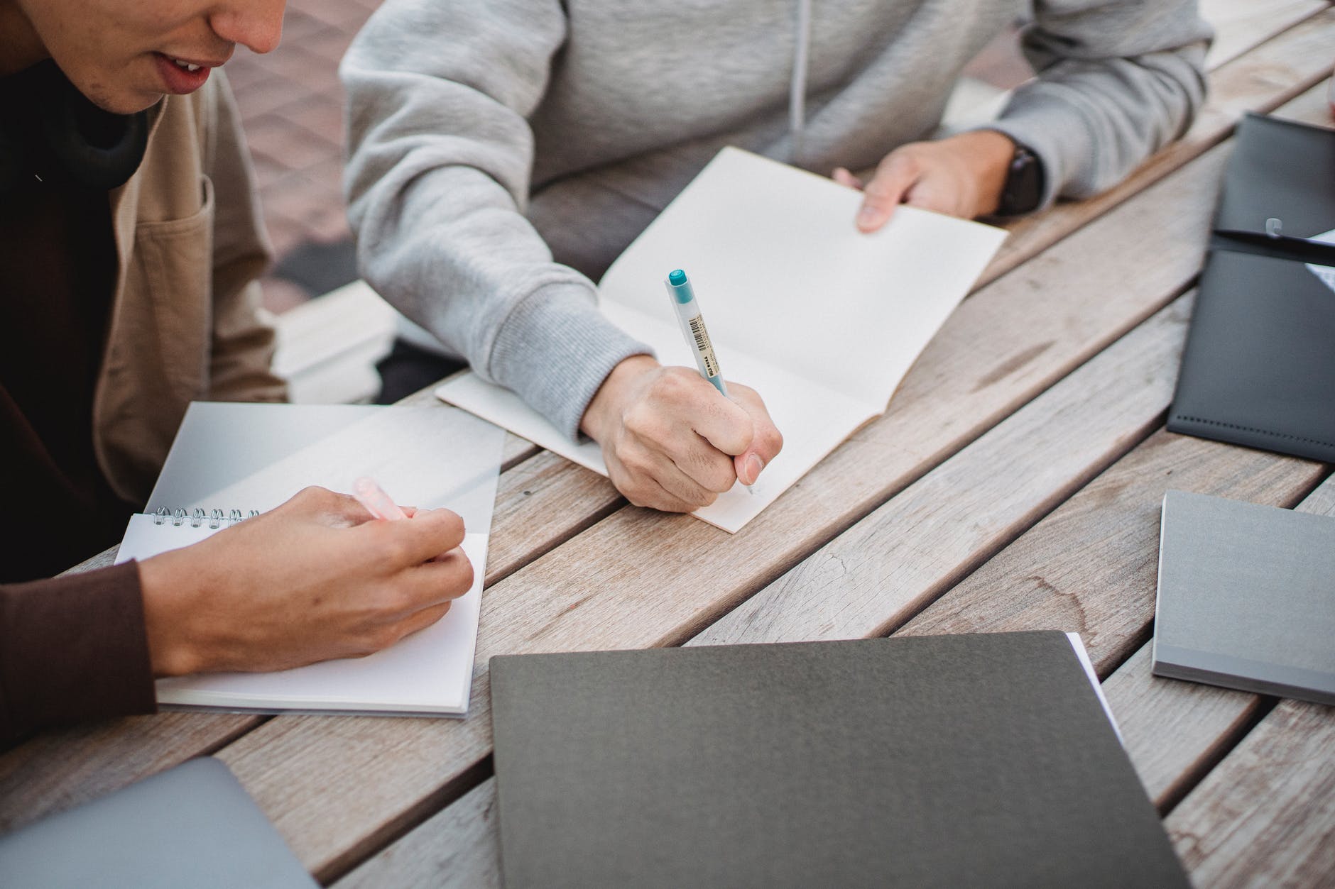 Two people writing on note pads on wood table.