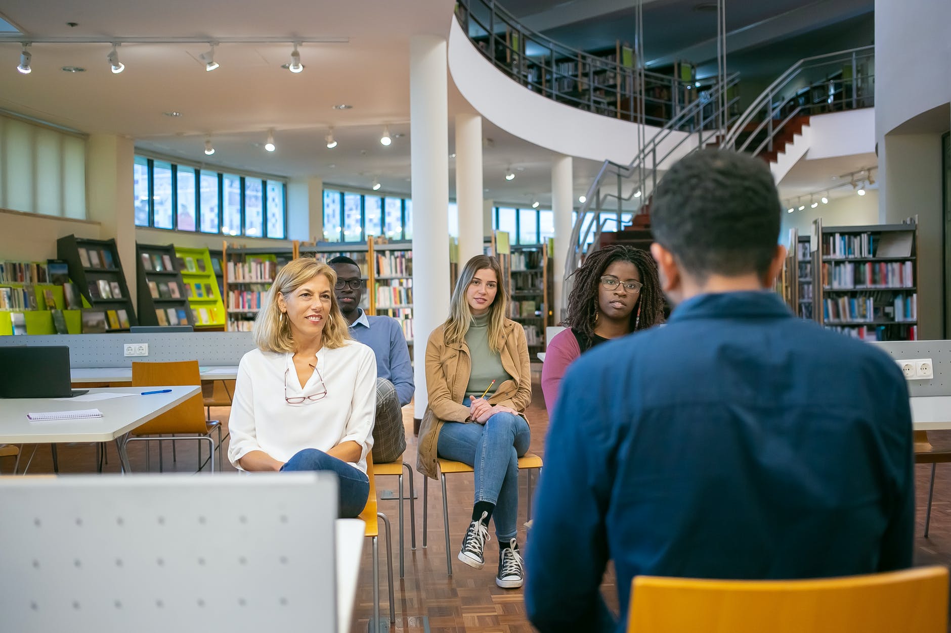 Group of people at library watching/listening to person with back facing camera.