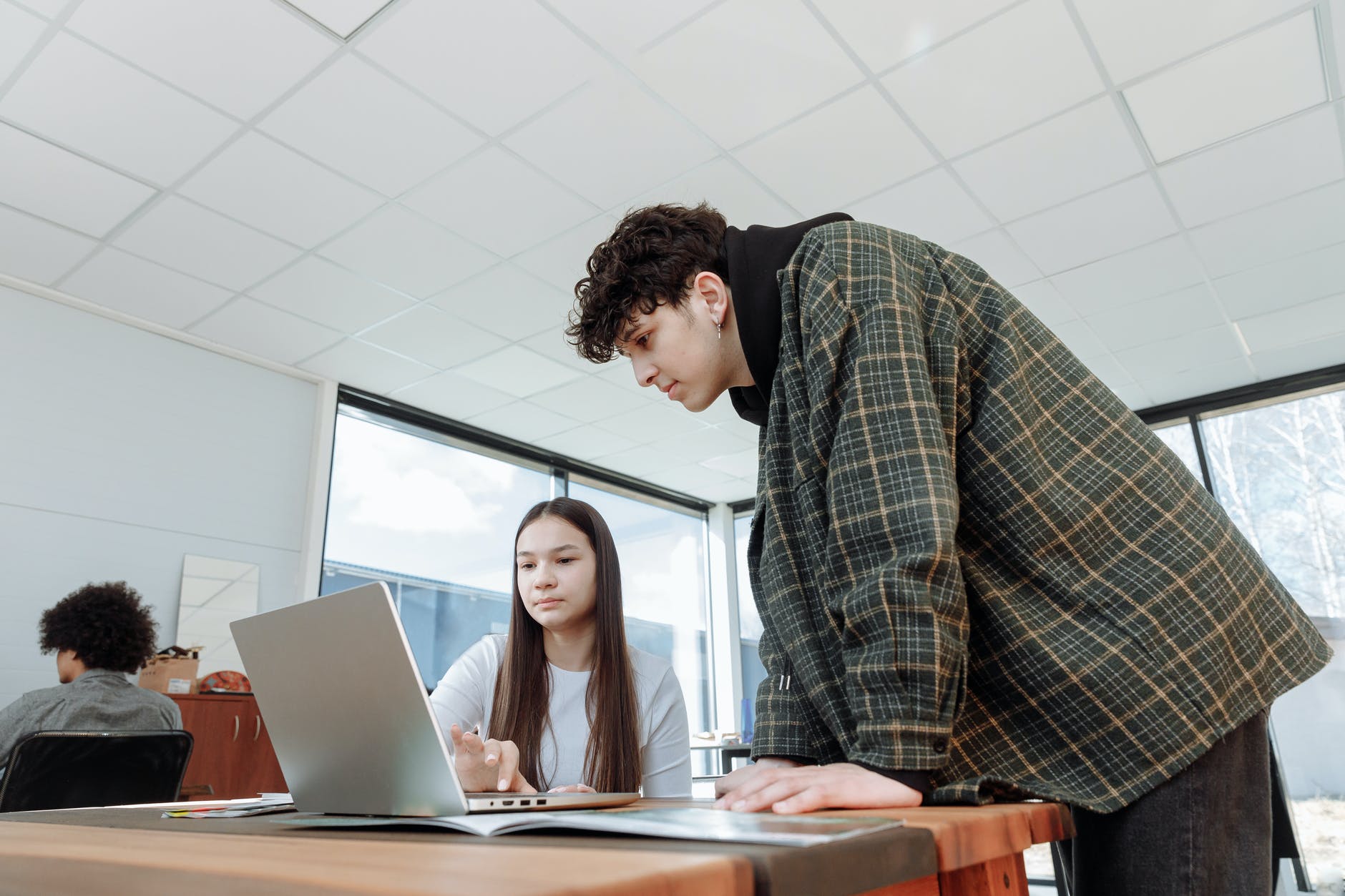 Woman using laptop on desk with man standing and looking at screen.