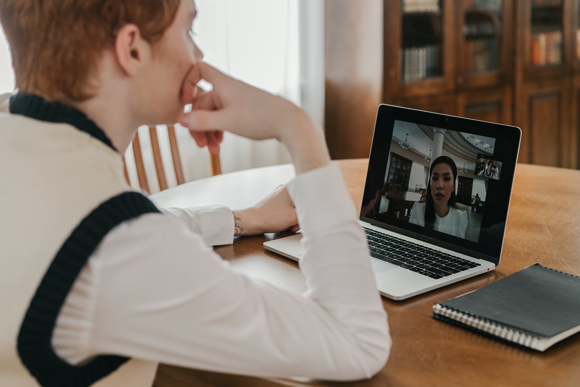 Person at round table using laptop for video conferencing. Woman can be seen on screen of laptop.