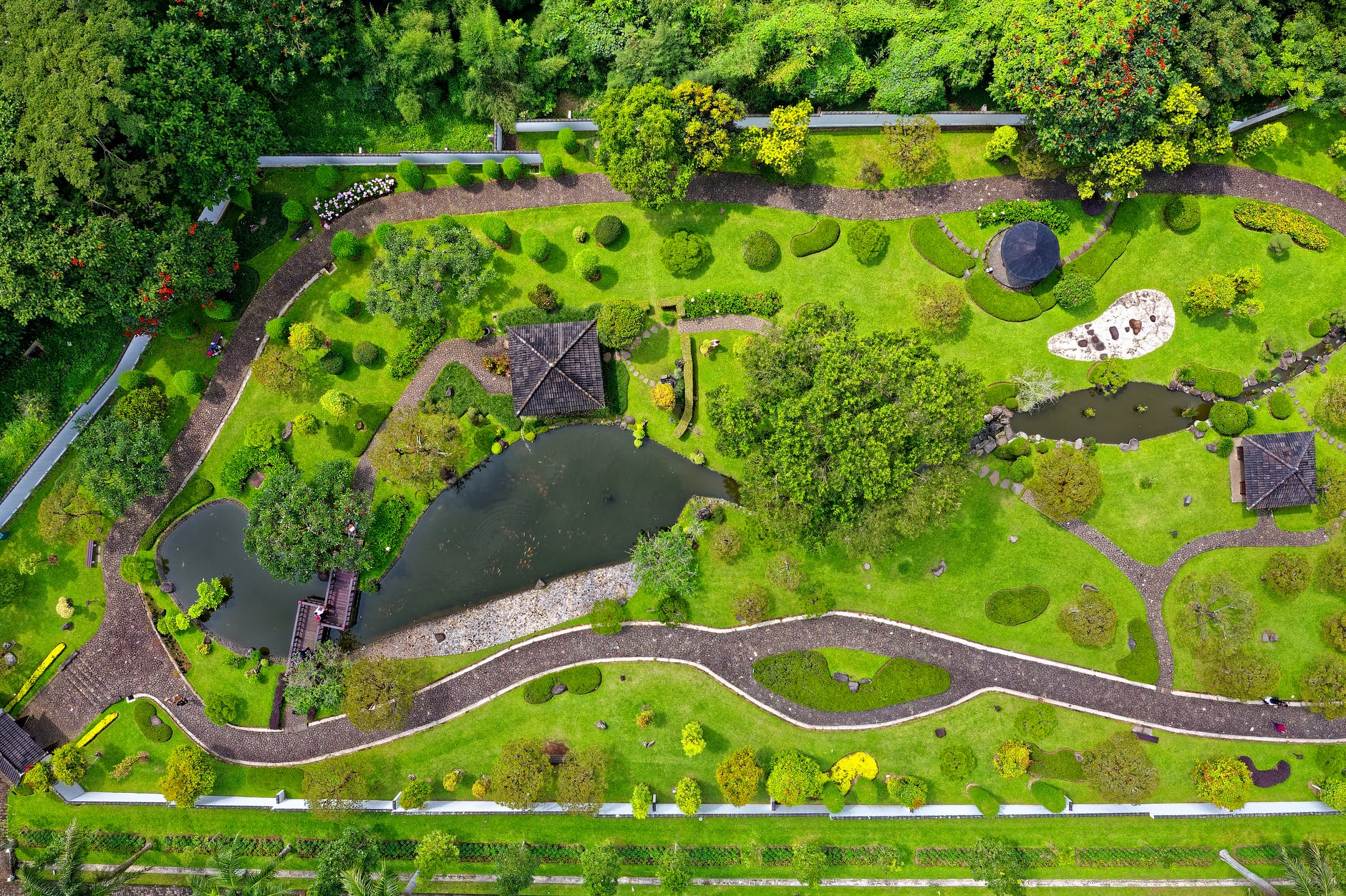 Aerial view of green landscape with trees, a lake, and paths.
