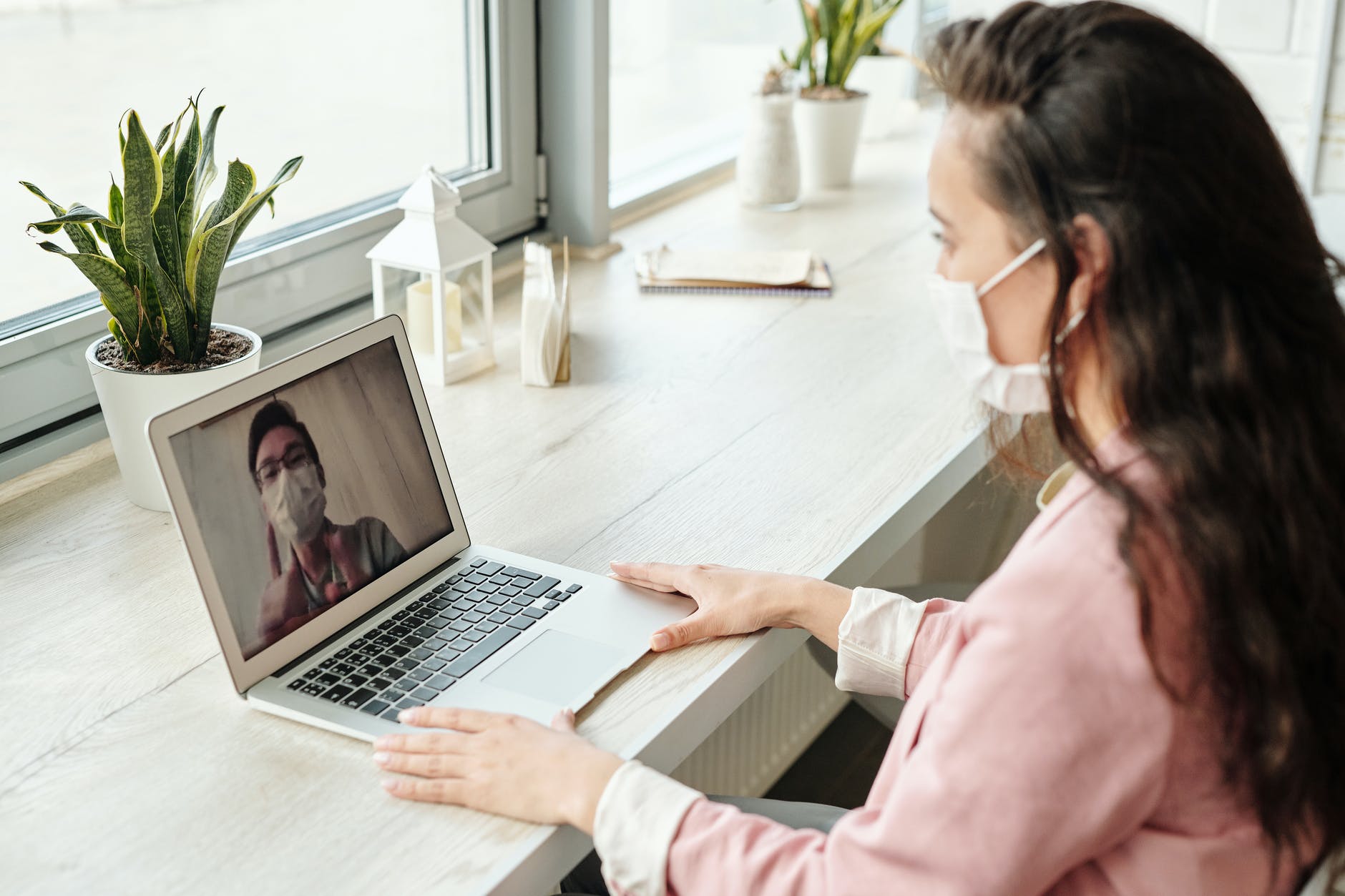 woman wearing a mask working on laptop. Man on screen is also wearing a mask.