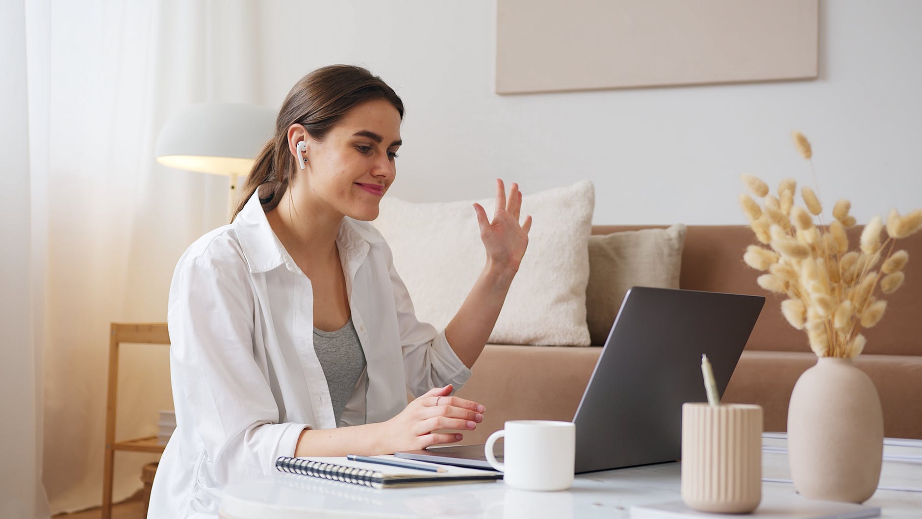 Woman with ponytail waving at someone on laptop screen.