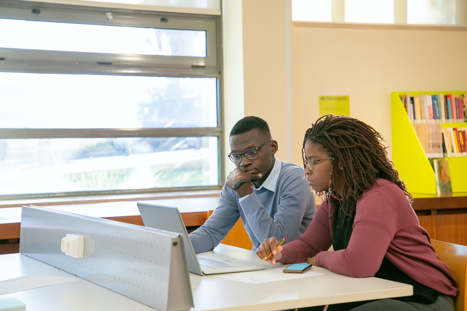 Black man and woman seated and working on laptop. They are both looking at the screen.