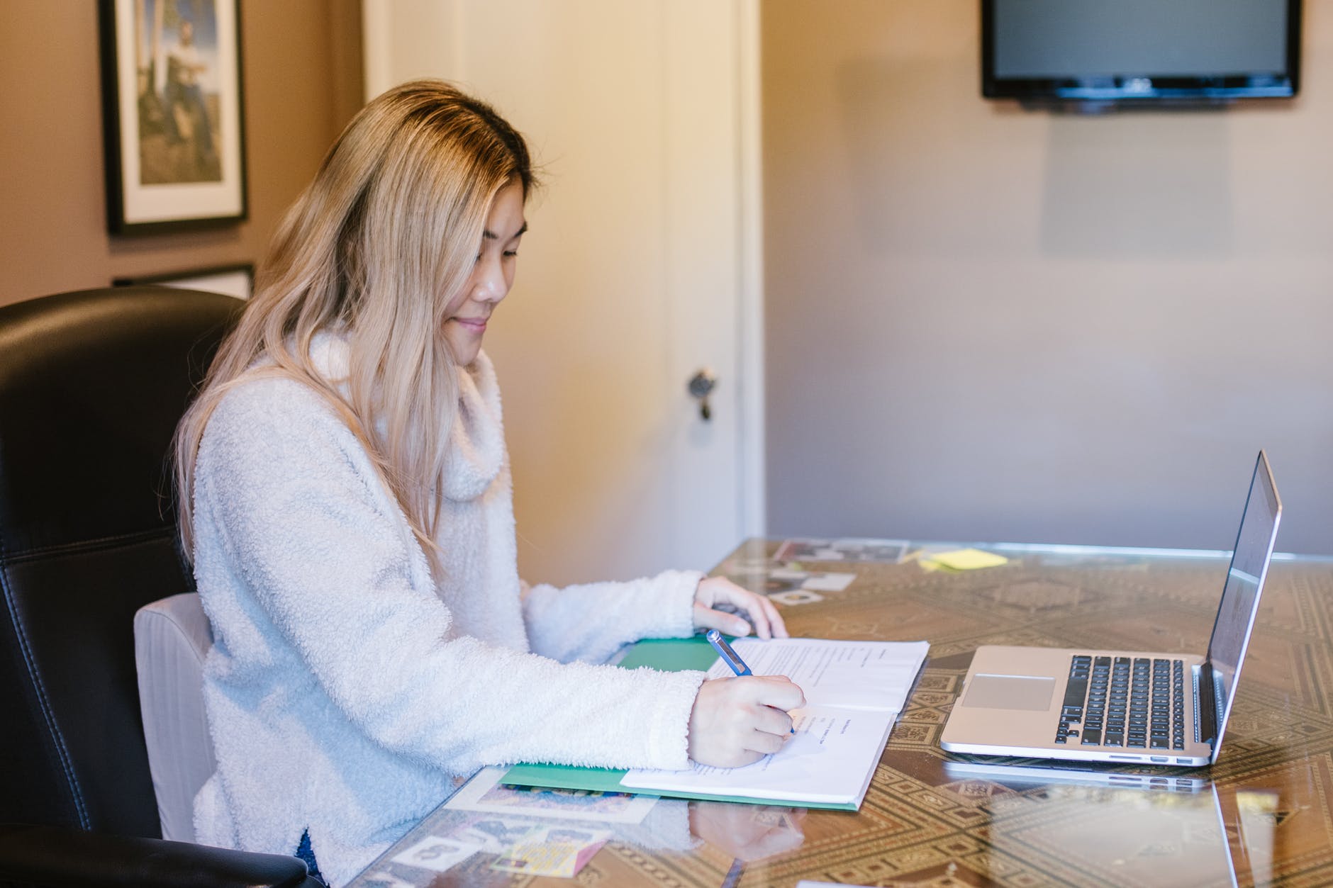 Blonde student writing in notebook in front of laptop.