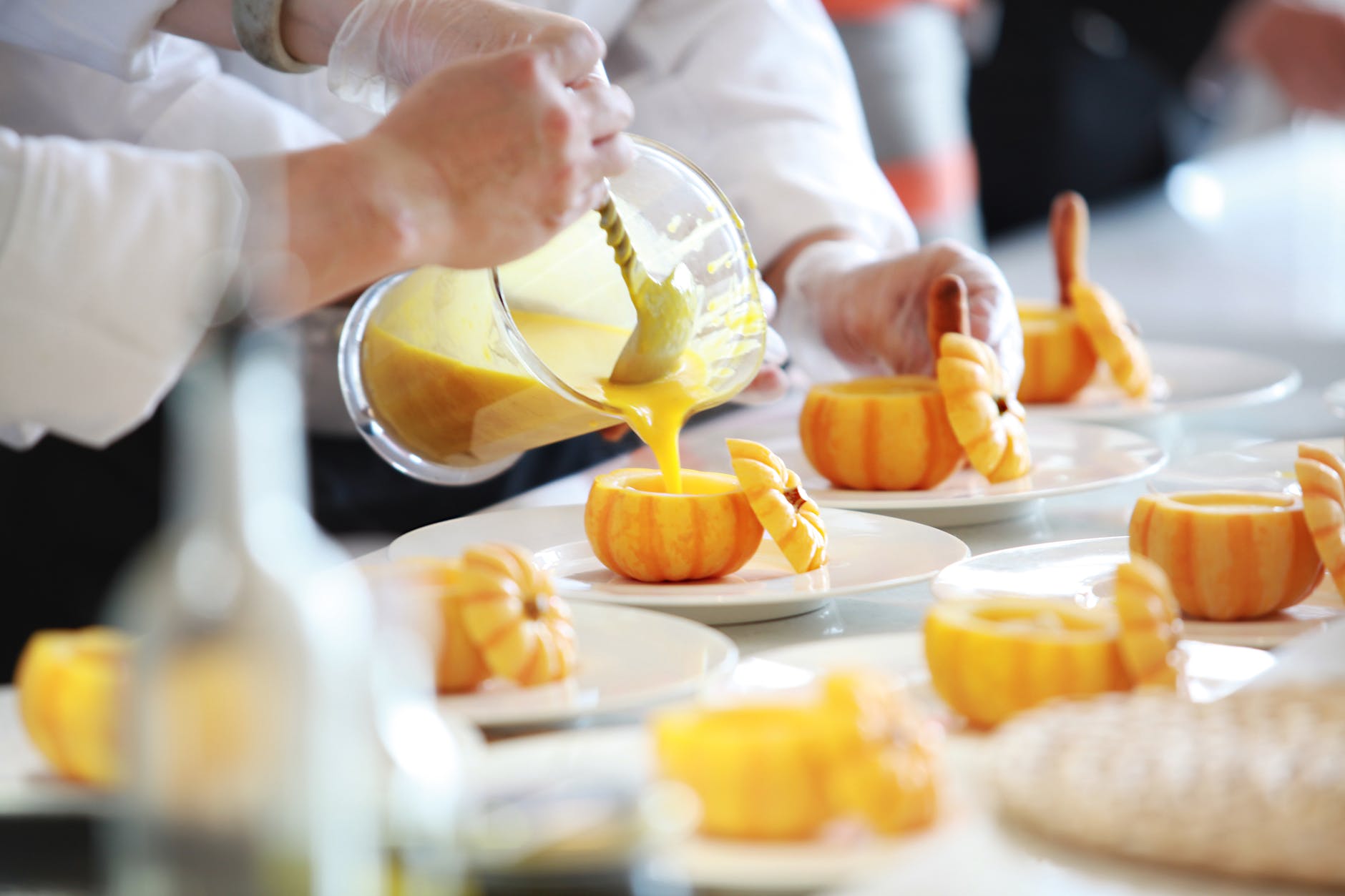 Chef's hands pouring yellow substance into pumpkin shaped pastires.