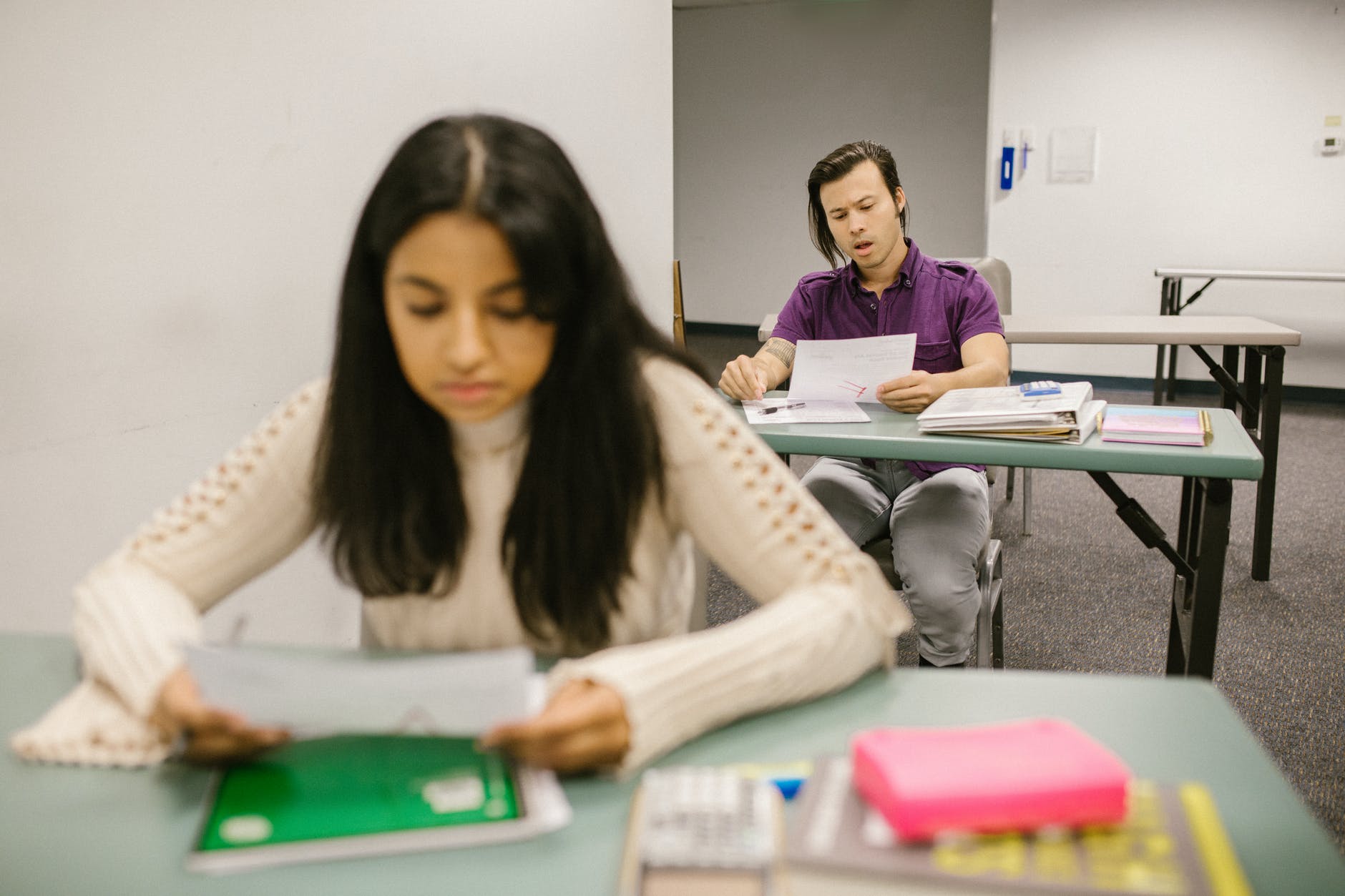 Woman looking at paper seated at desk. Behind her, a male student stares at an F on paper.