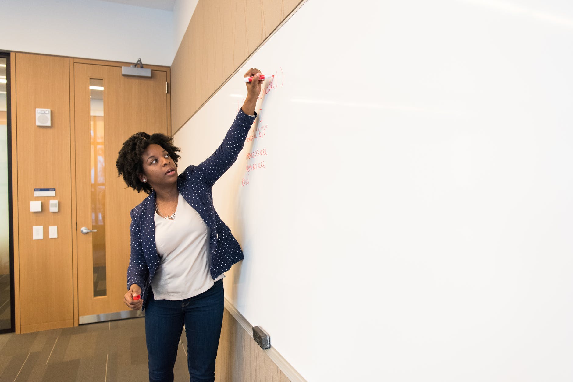 Black woman writing on whiteboard.