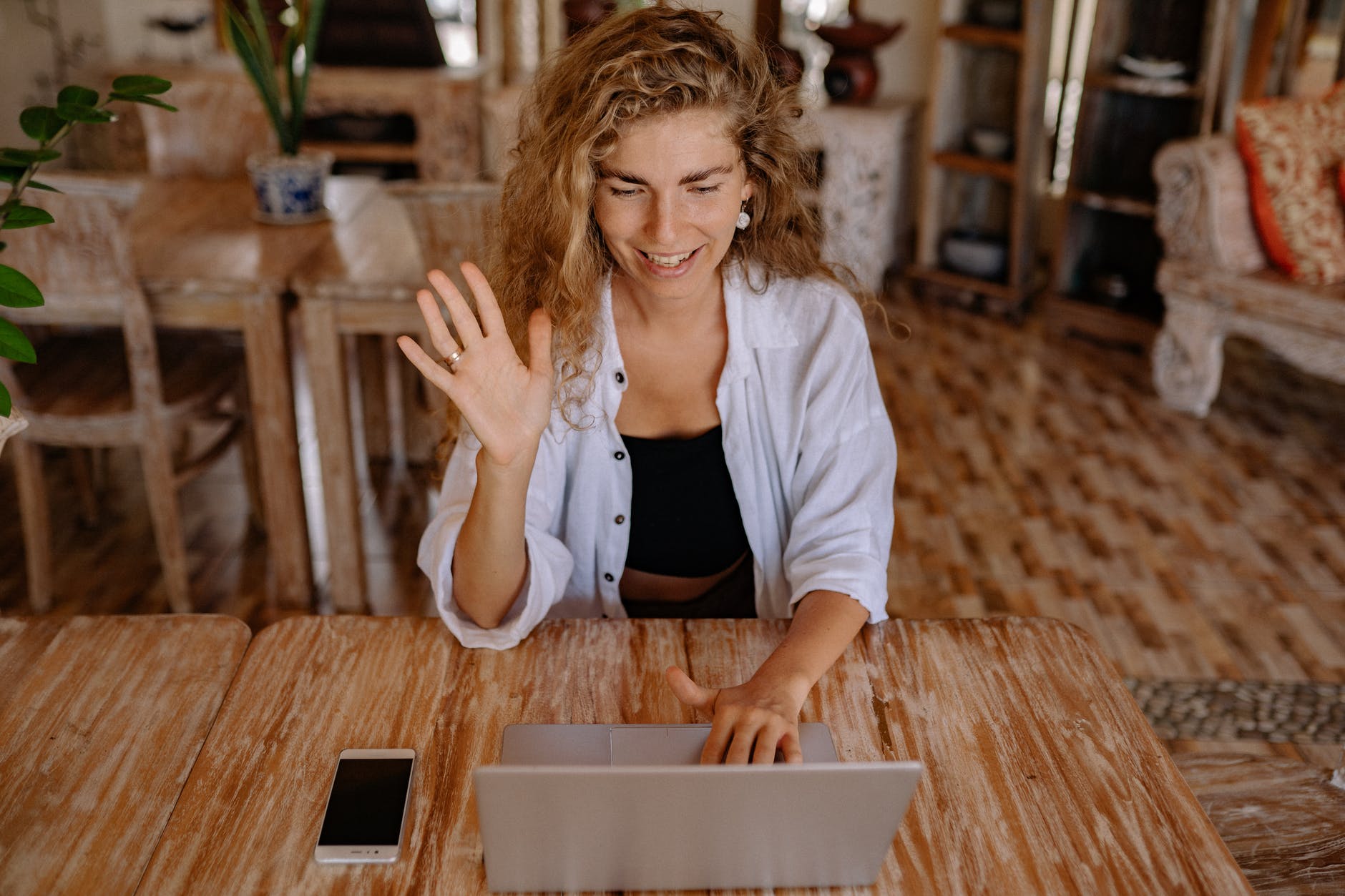 Woman with curly blond/brown hair waiving at computer.