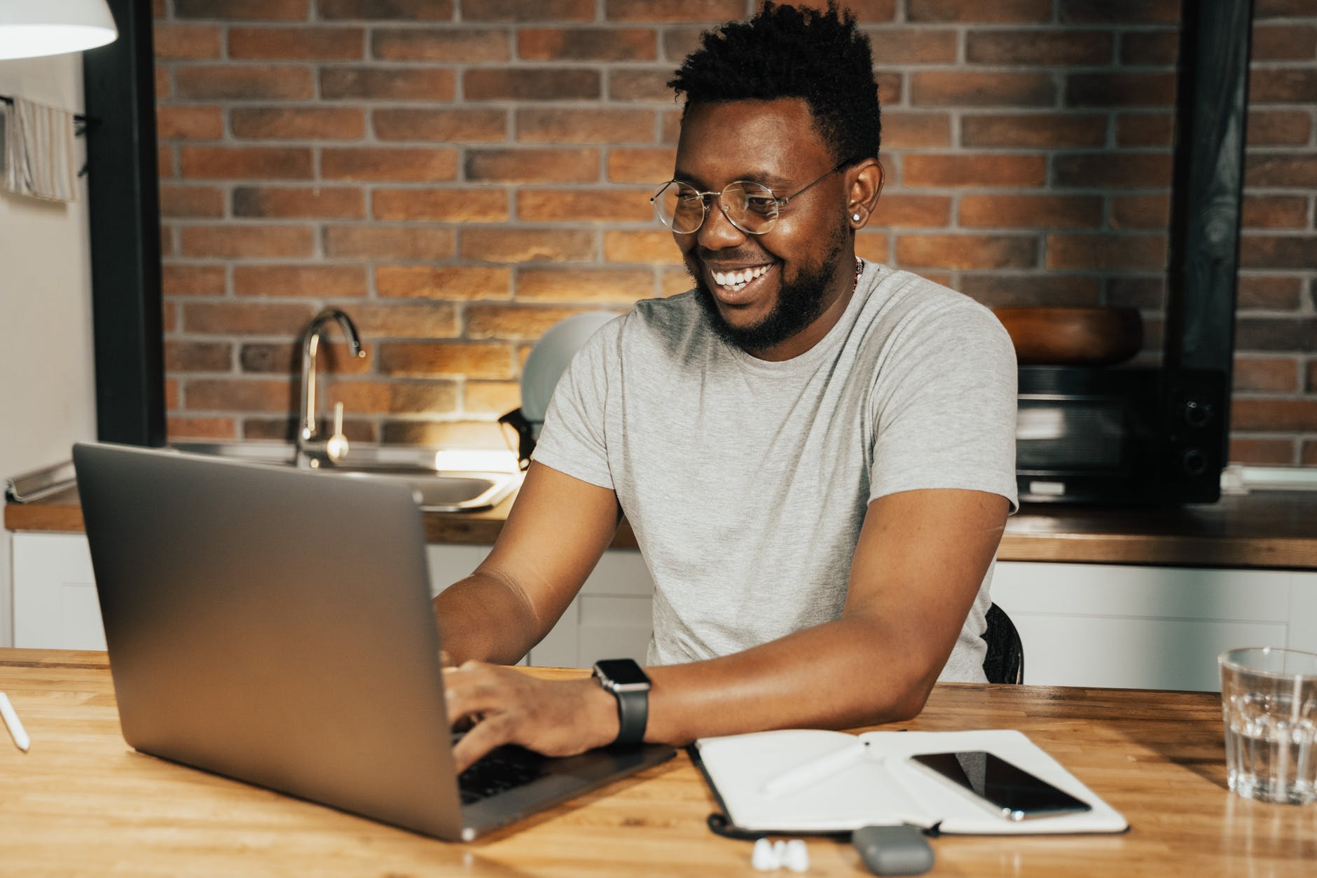 Black man with short beard wearing glasses and a gray t-shirt and working on laptop.