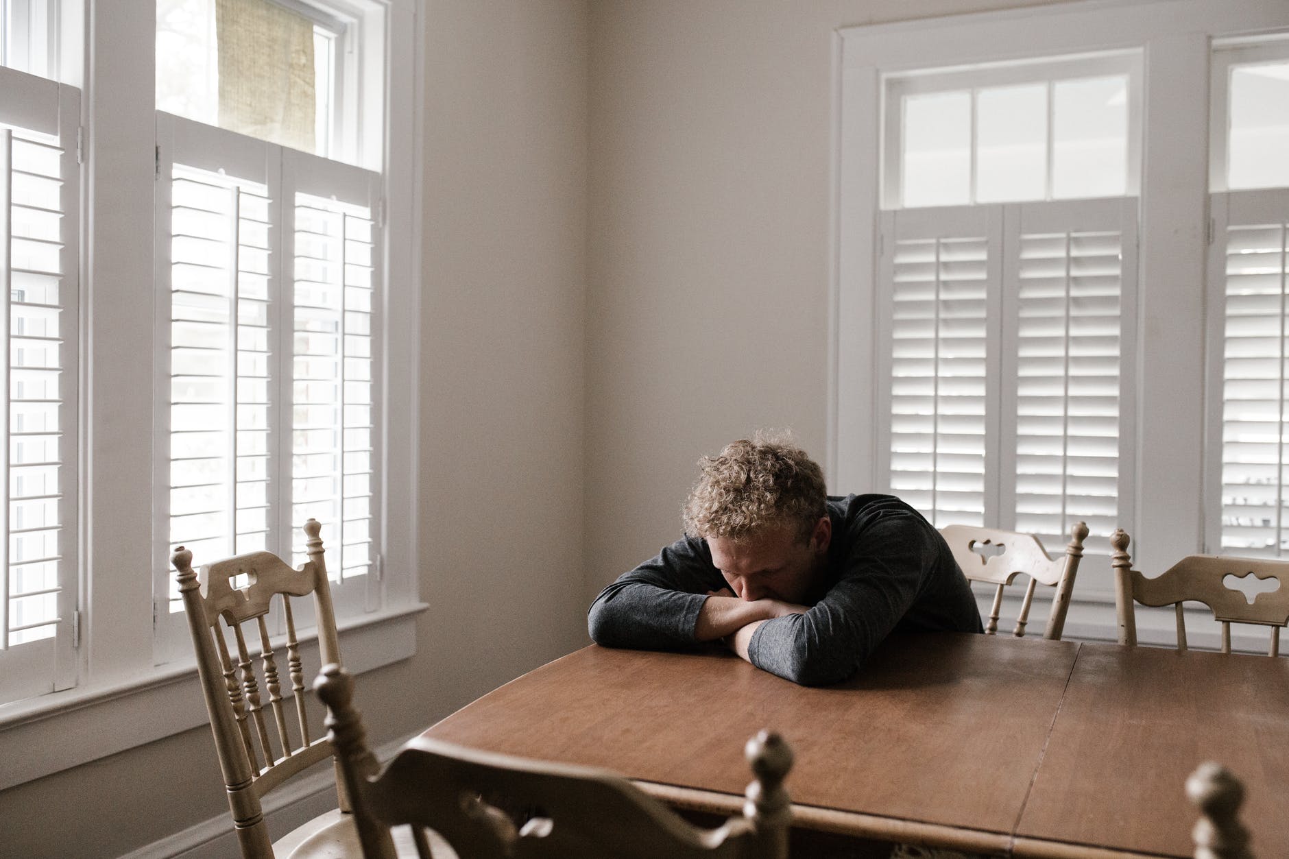 Man at table in empty room with arms on table staring down.
