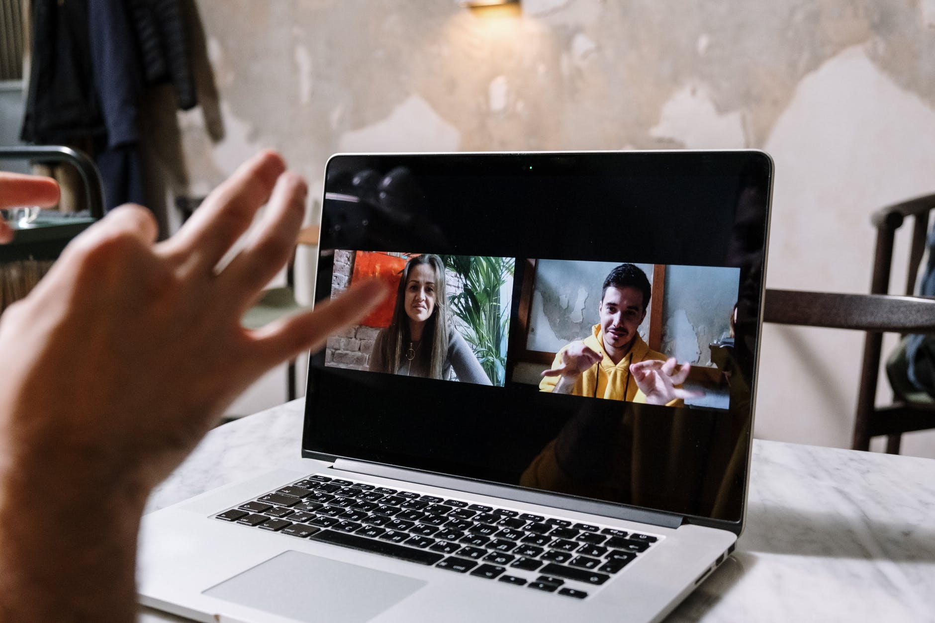 Laptop screen with two video feed: a woman on the left and a man on the right using hands and fingers to communicate.