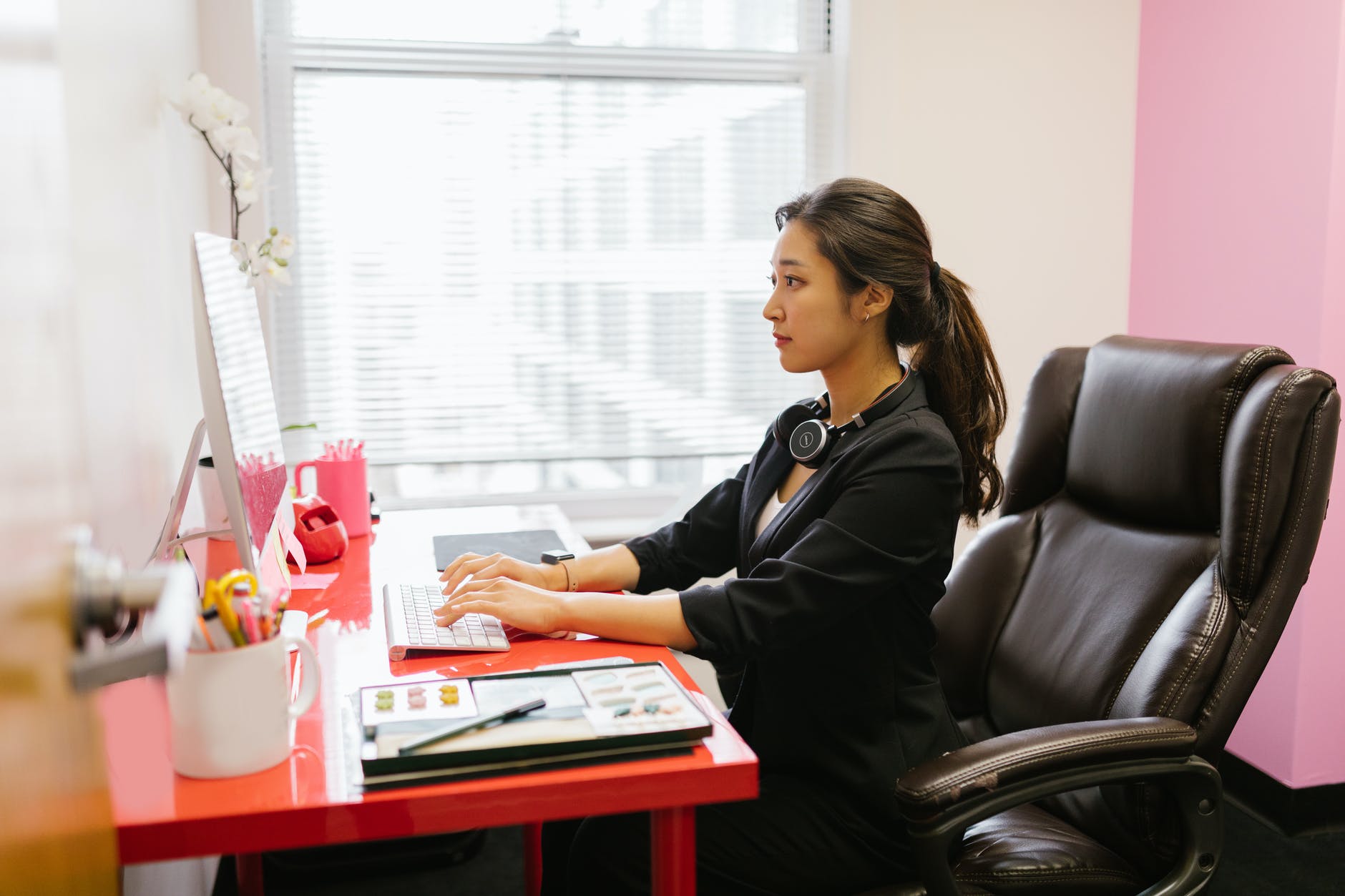 Woman seated at red desk typing on desktop computer.
