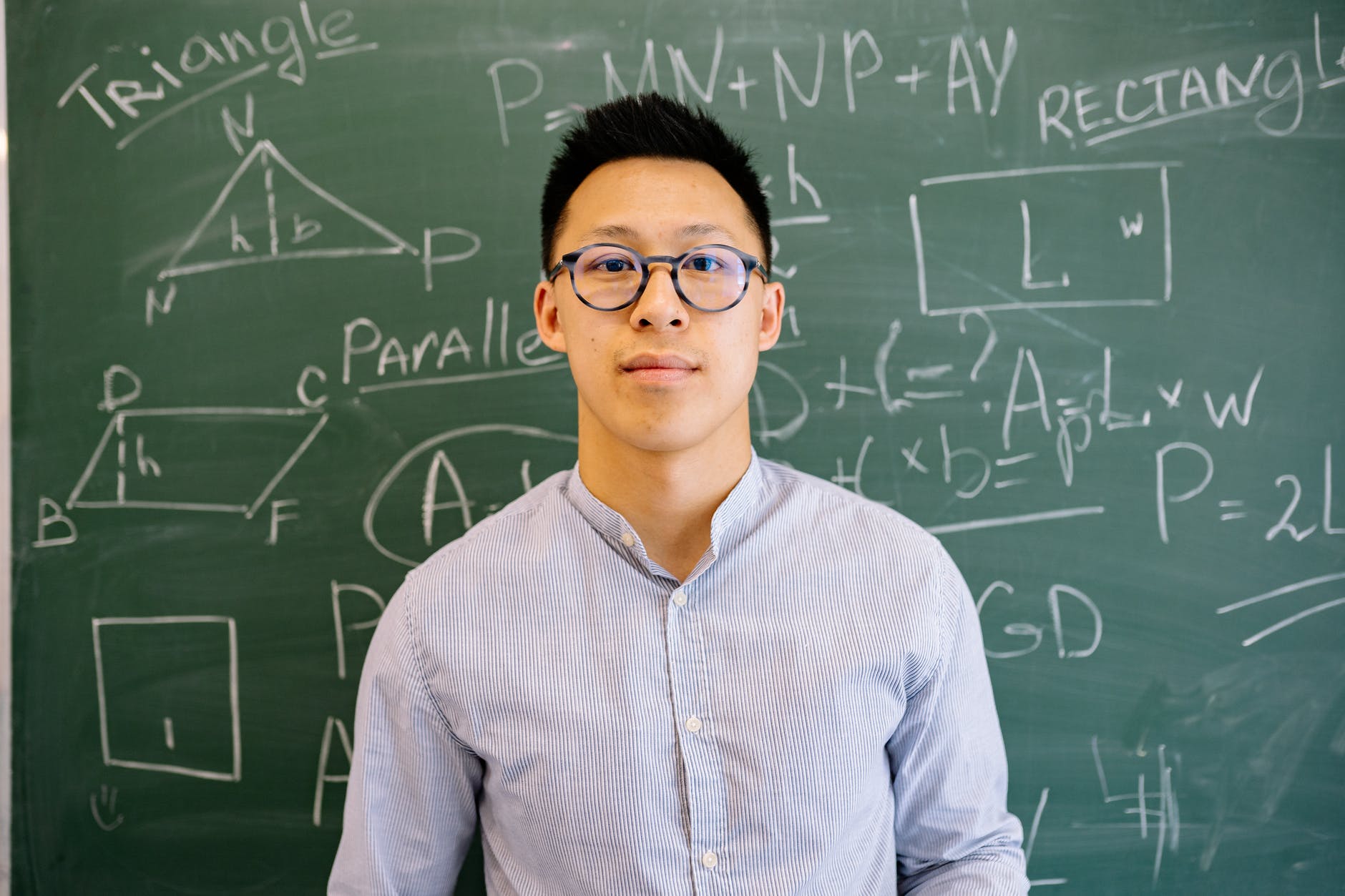 Asian man with glasses. Blackboard with formulas written in white chalk in the background.