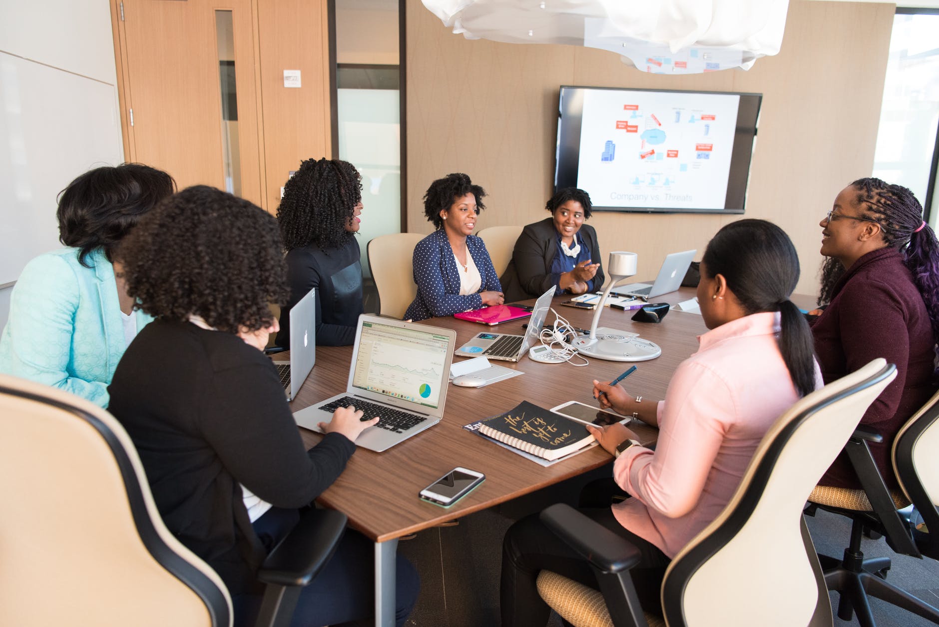 Group of black women around conference table with screens and A/V equipment.