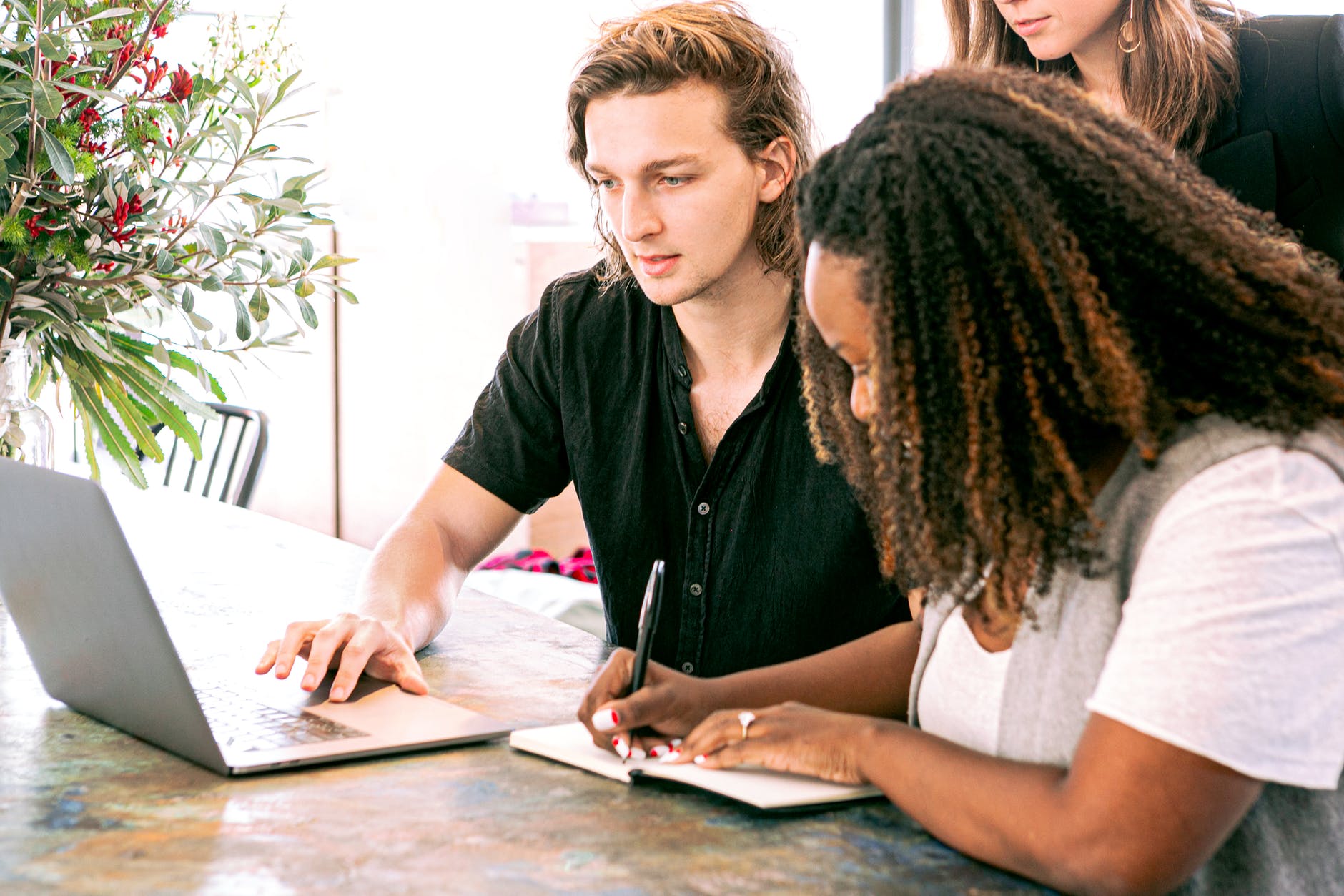 Man with shoulder length brown hair and black woman with curly hair working on laptop.