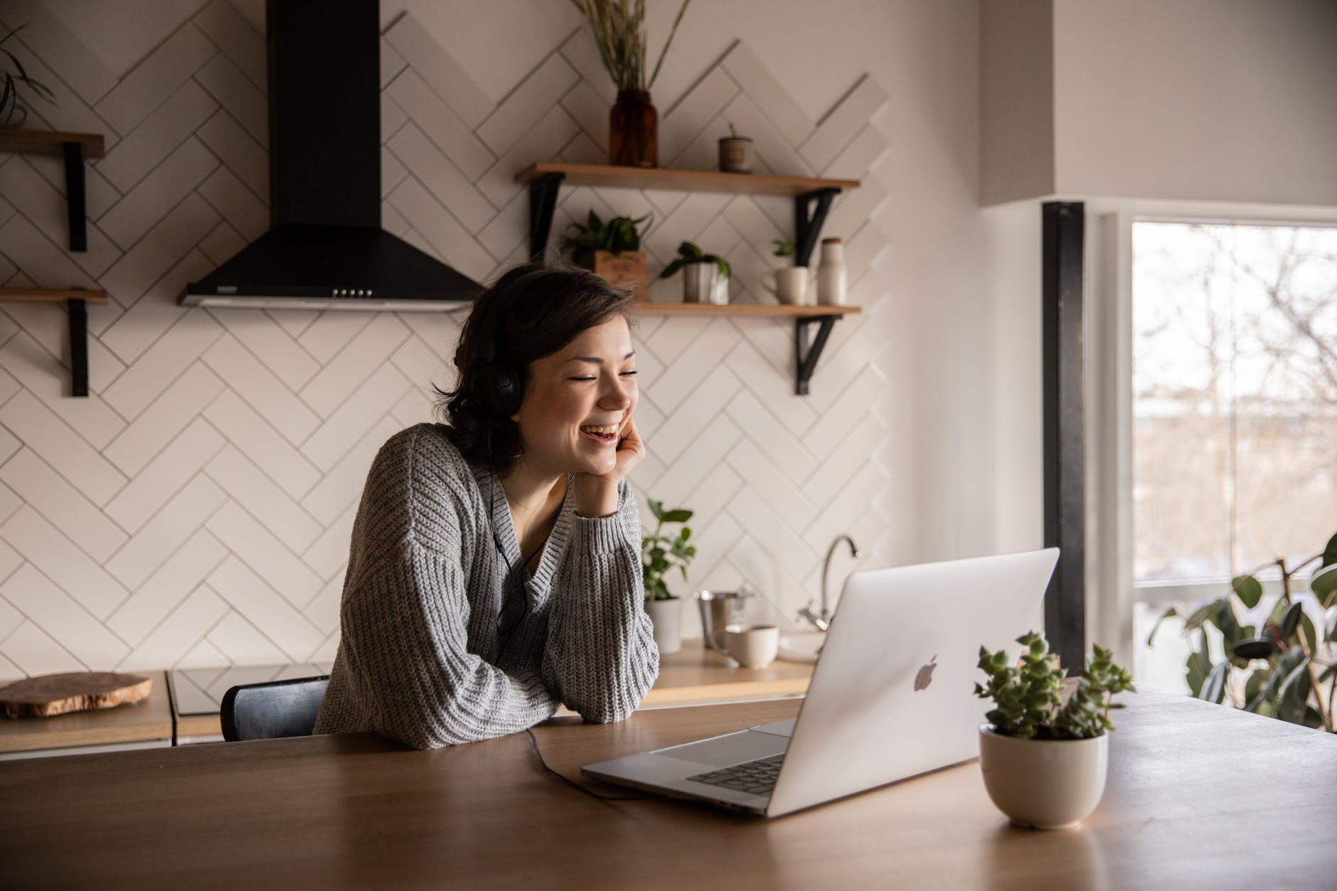 Woman in kitchen table working on laptop and smiling.